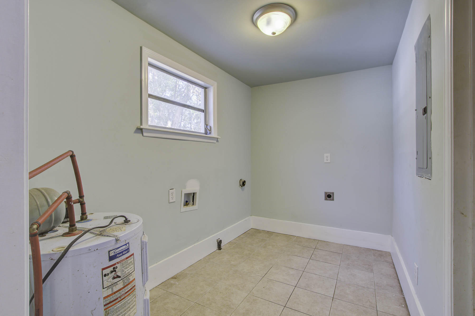 Empty laundry room with beige tile, washer hookups, a small window, and a water heater.