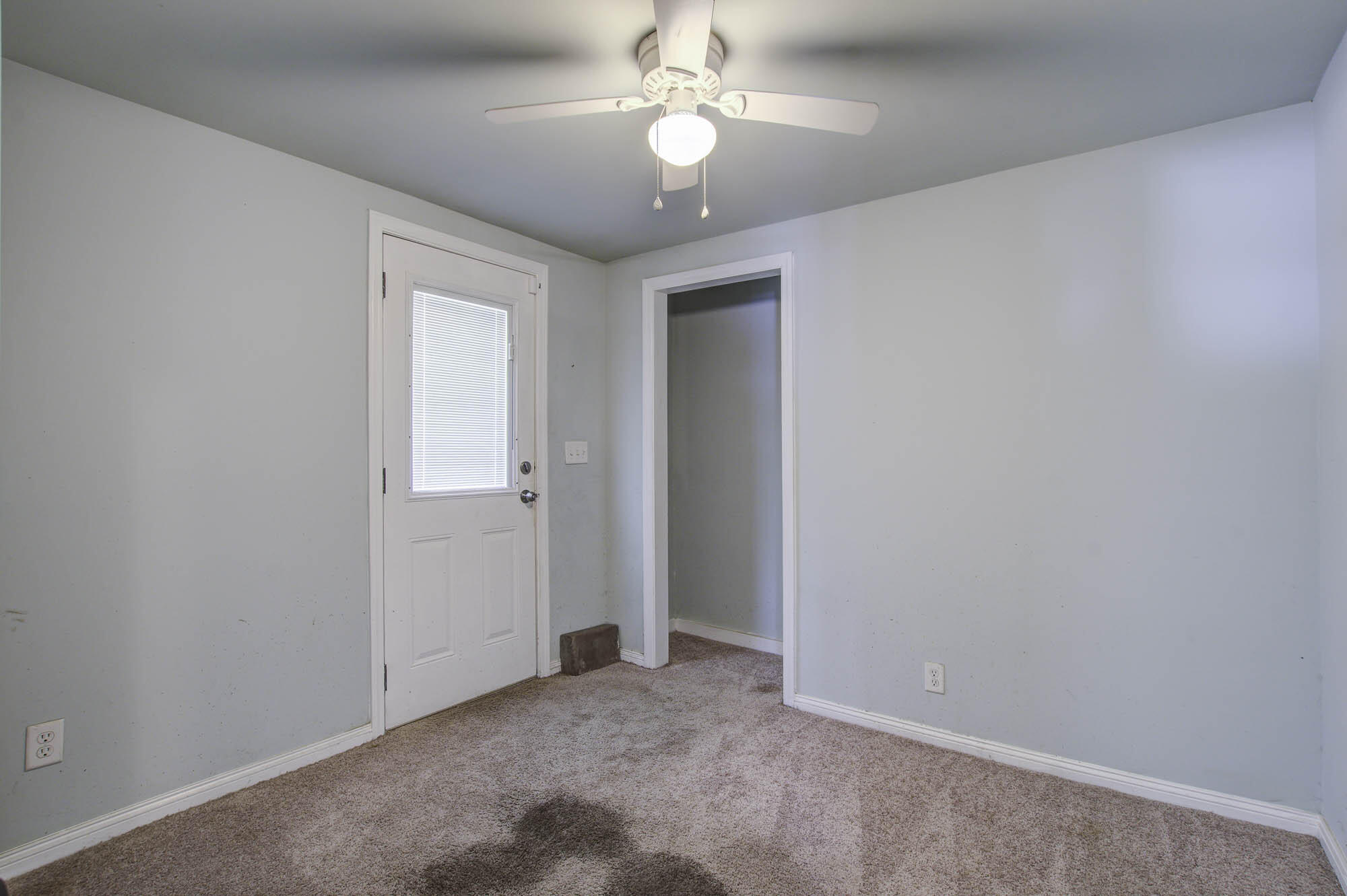 Empty carpeted room with pale blue walls, a white door with blinds, and a ceiling fan.