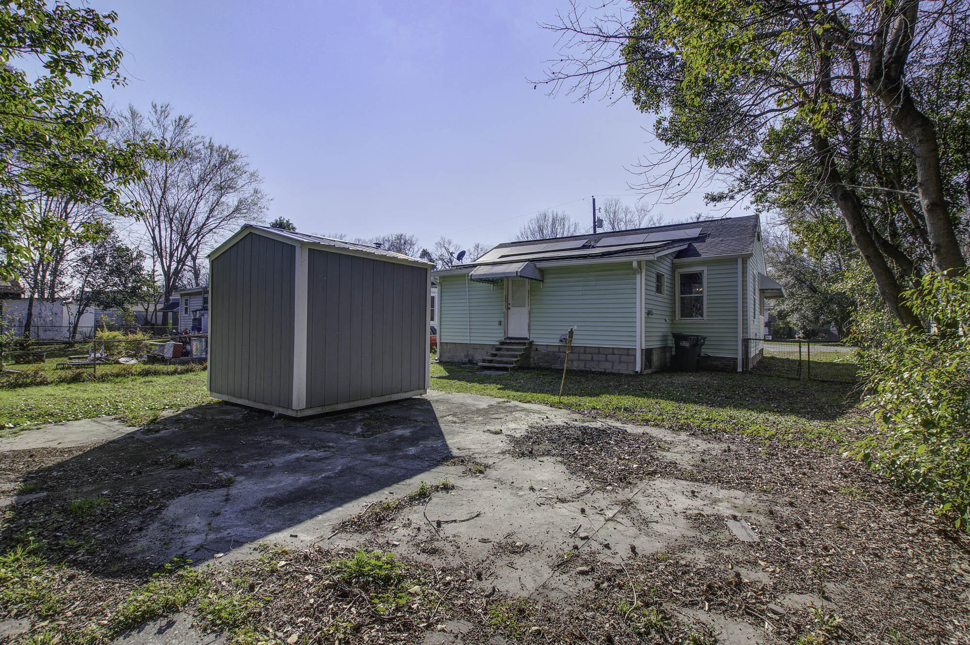 Rear of a light green home with rooftop solar panels, a large shed, and a concrete patio.
