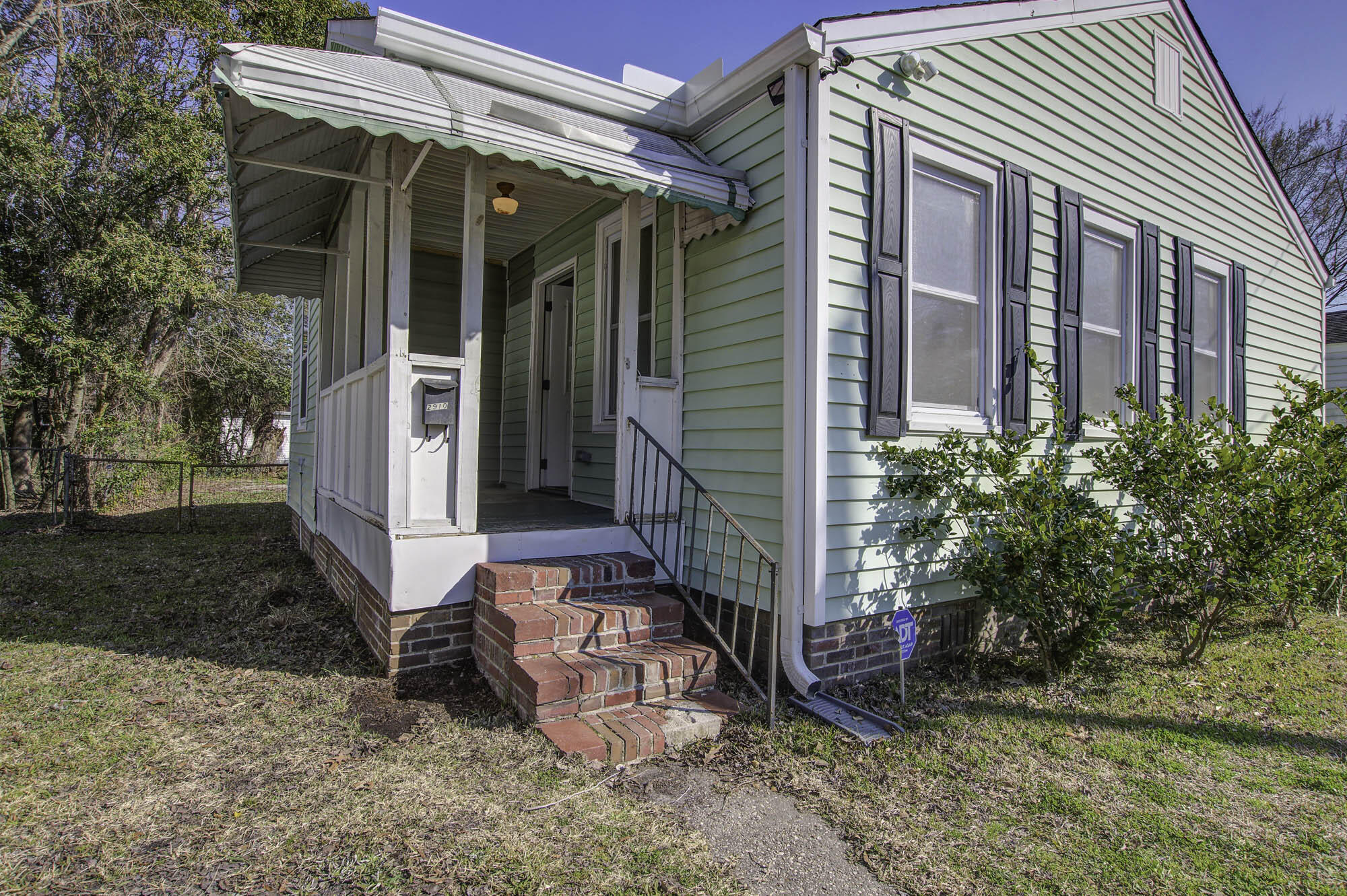 Pale green house with dark shutters, a covered porch, and brick front steps.