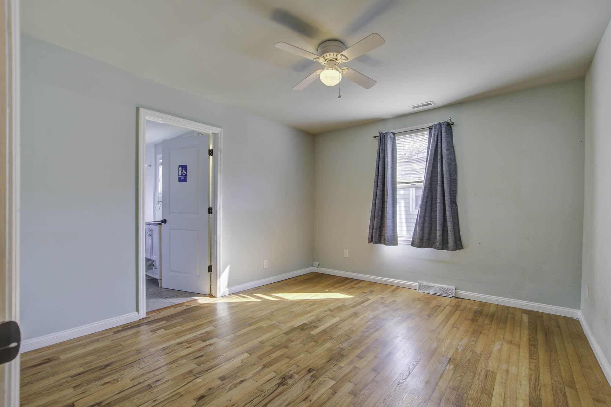 Empty bedroom with hardwood floors, a ceiling fan, and an open doorway to a bathroom.