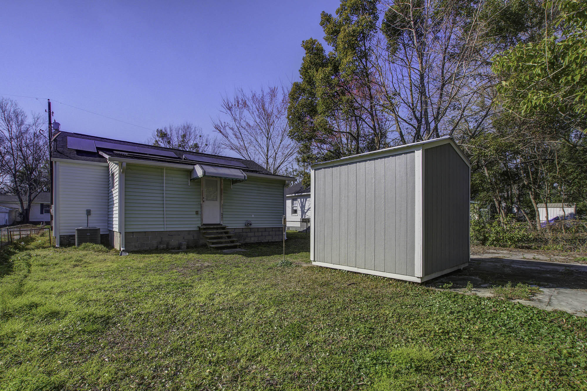 Rear of a light-sided house with rooftop solar panels and a large gray shed in the yard.