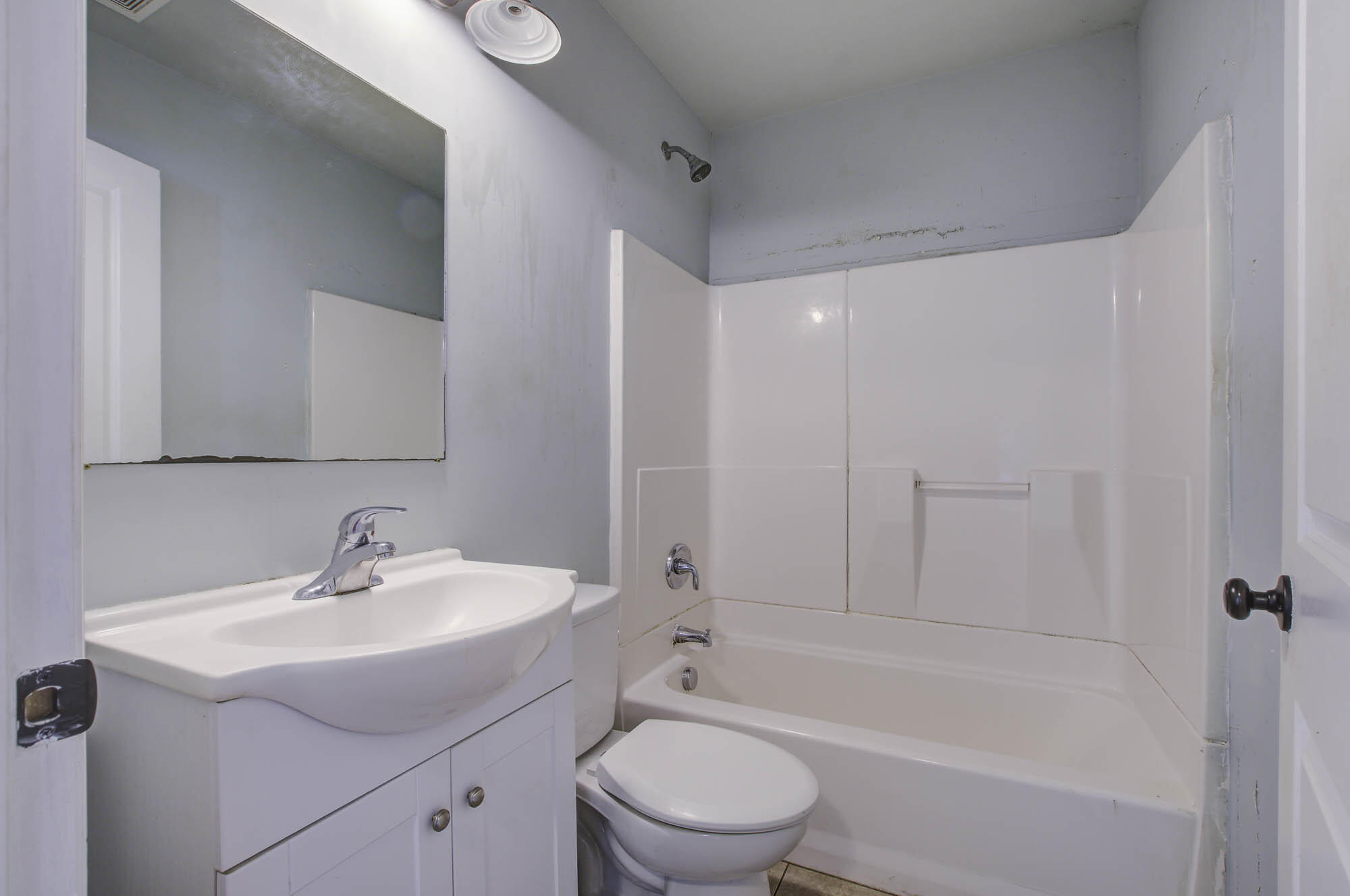 Bathroom with a white bathtub and shower, toilet, and vanity with a large mirror.