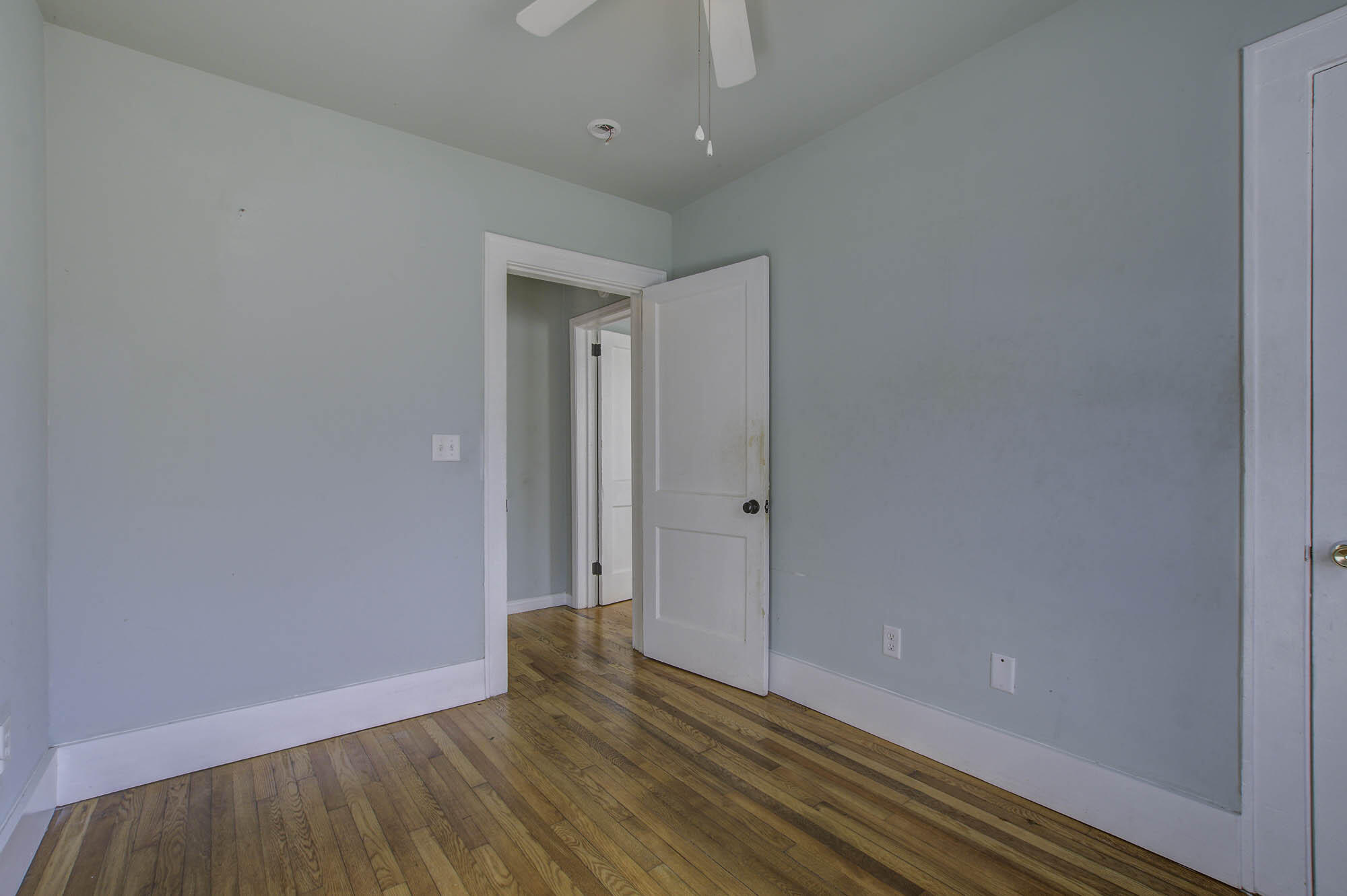 Empty bedroom with pale blue walls, hardwood floors, and an open white door.