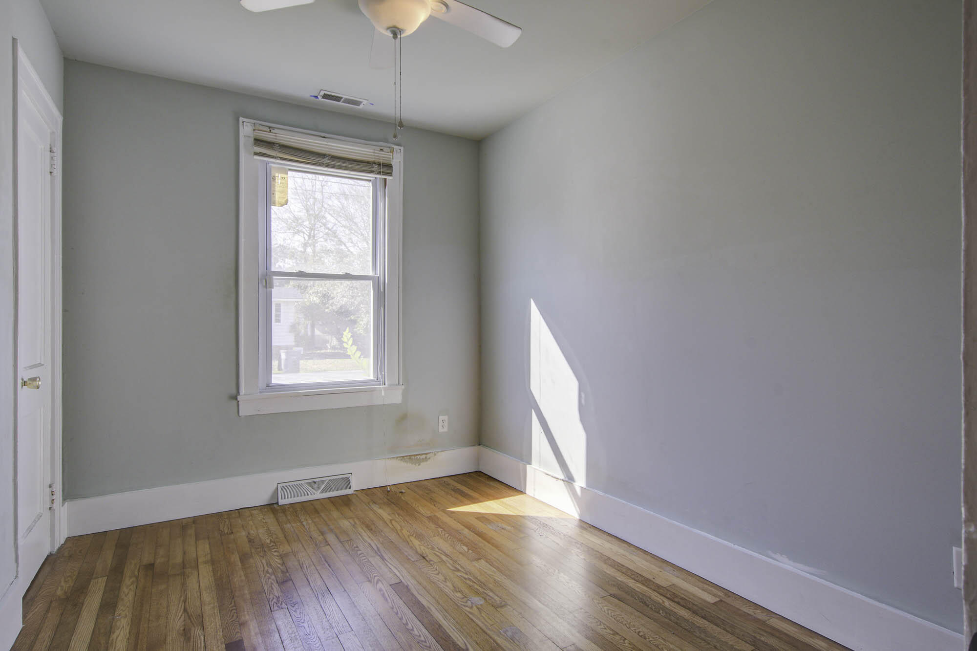 Vacant room with hardwood floors, a window with blinds, and sunlight across the floor.