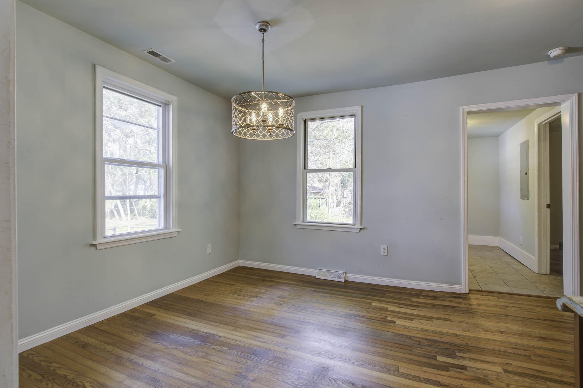Empty dining room with hardwood floors, two windows, and a decorative pendant light.
