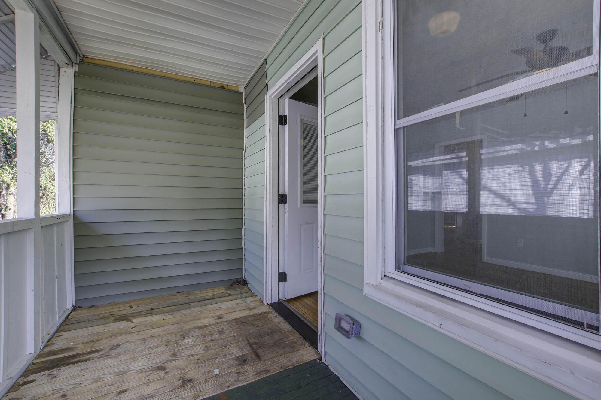 Covered porch with weathered wood decking, white railing, and an open screen door.
