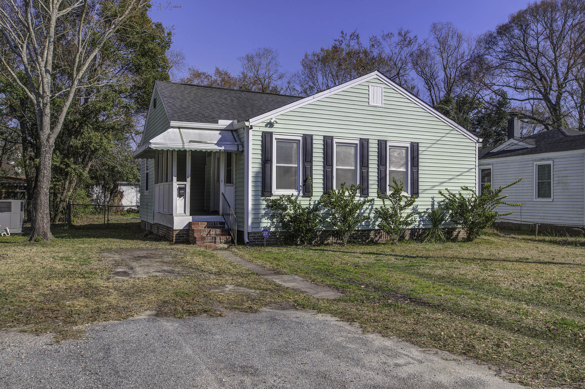 Light green single-story house with a covered porch, brick steps, and dark window shutters.