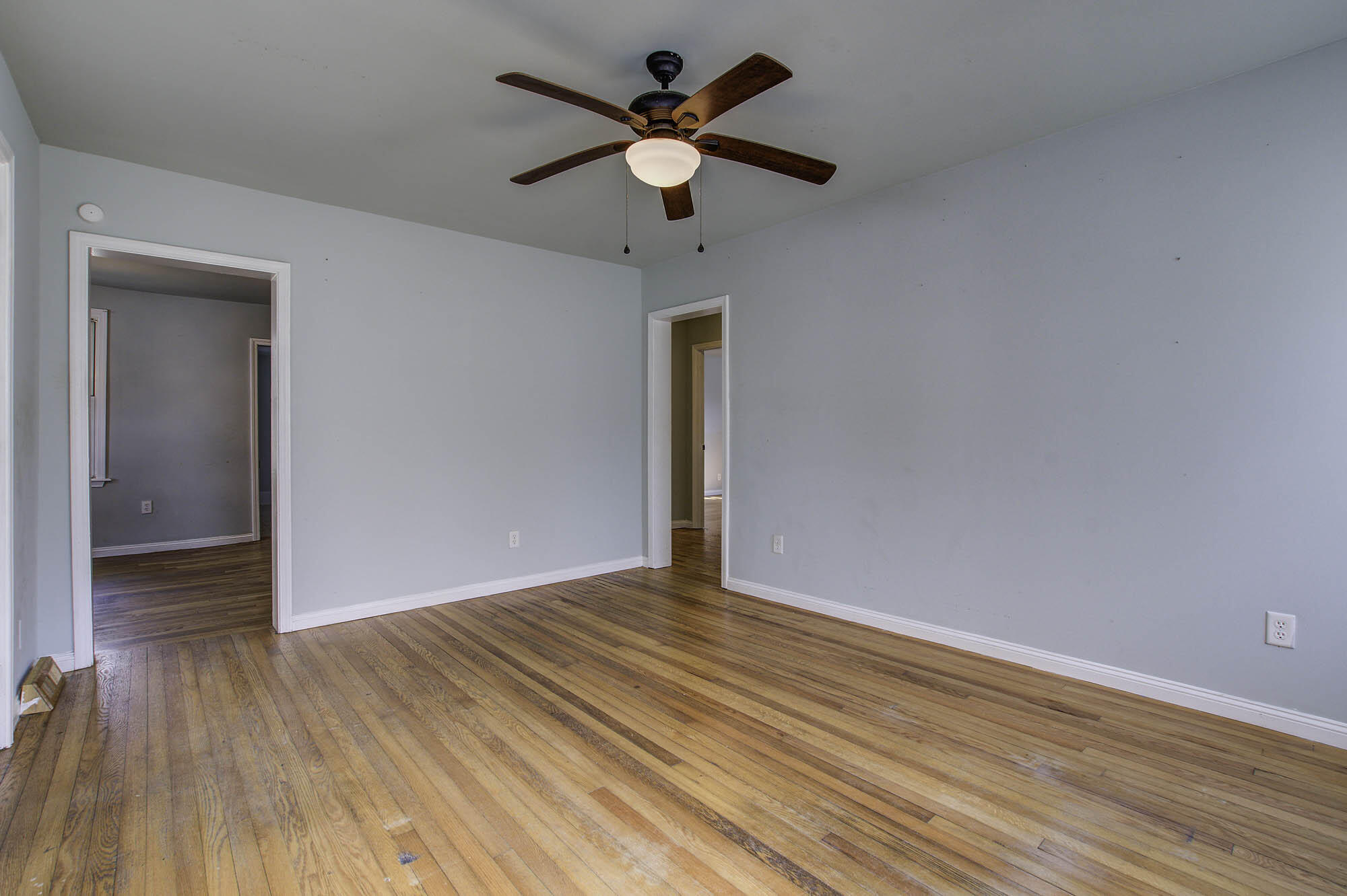 Empty room with hardwood floors, pale blue walls, and a wood-blade ceiling fan.
