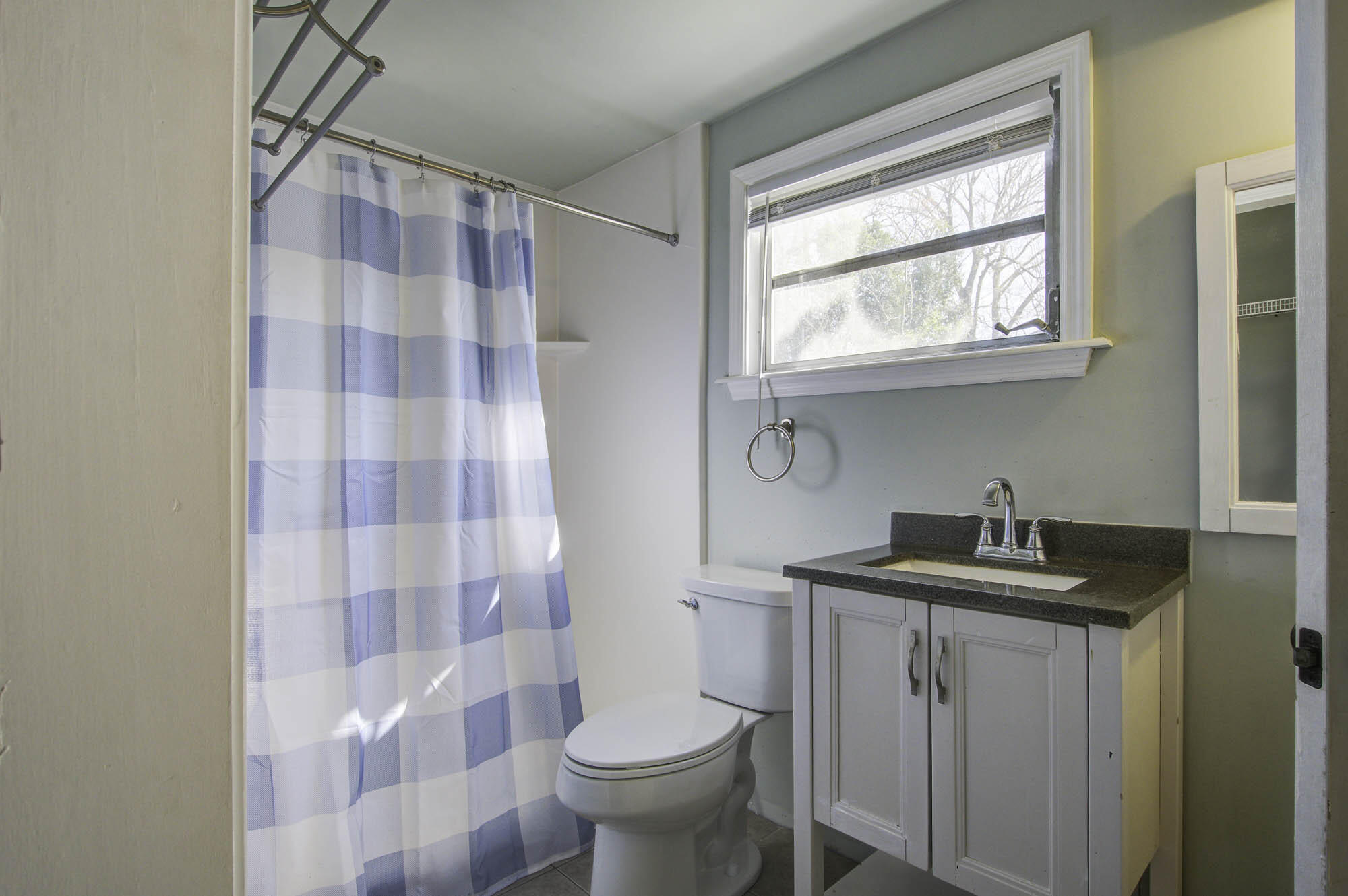 Bathroom with a blue-and-white striped shower curtain, toilet, and white vanity beneath a window.