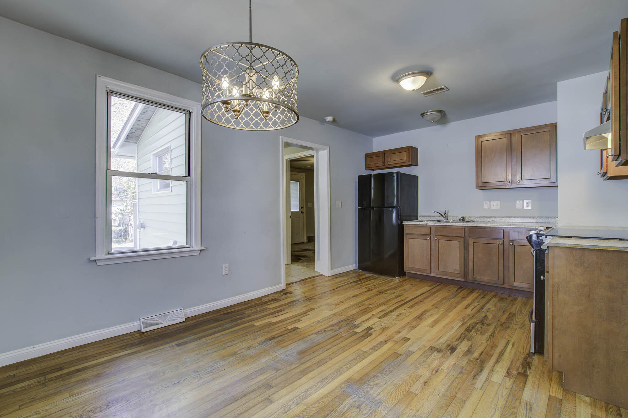 Kitchen with reddish wood cabinets, a black refrigerator, hardwood floors, and a patterned hanging light.