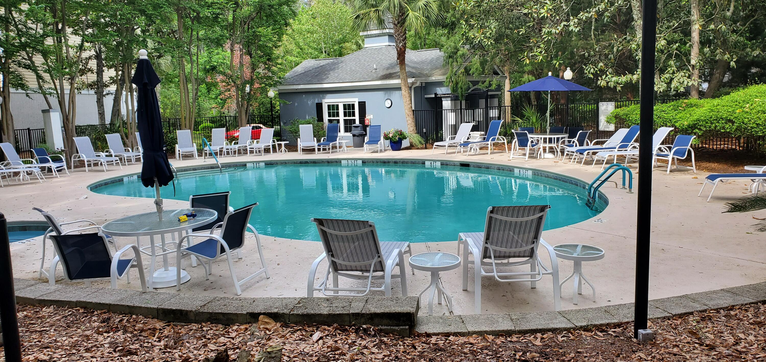 Outdoor pool with lounge chairs, blue umbrella, and leafy trees