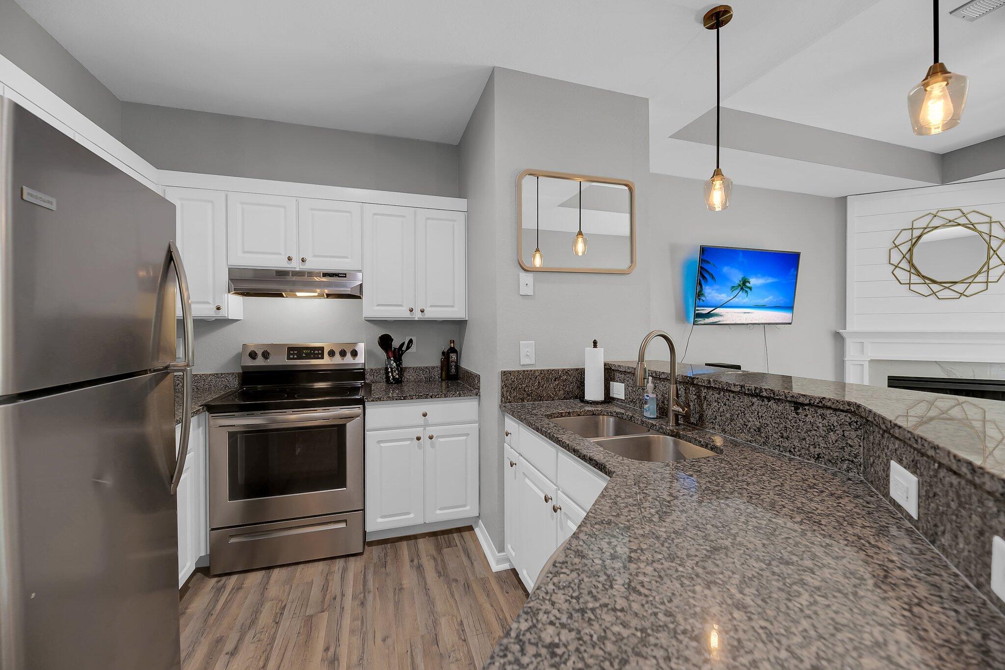 Updated kitchen with white cabinets, stainless steel appliances, granite counters, and pendant lights.