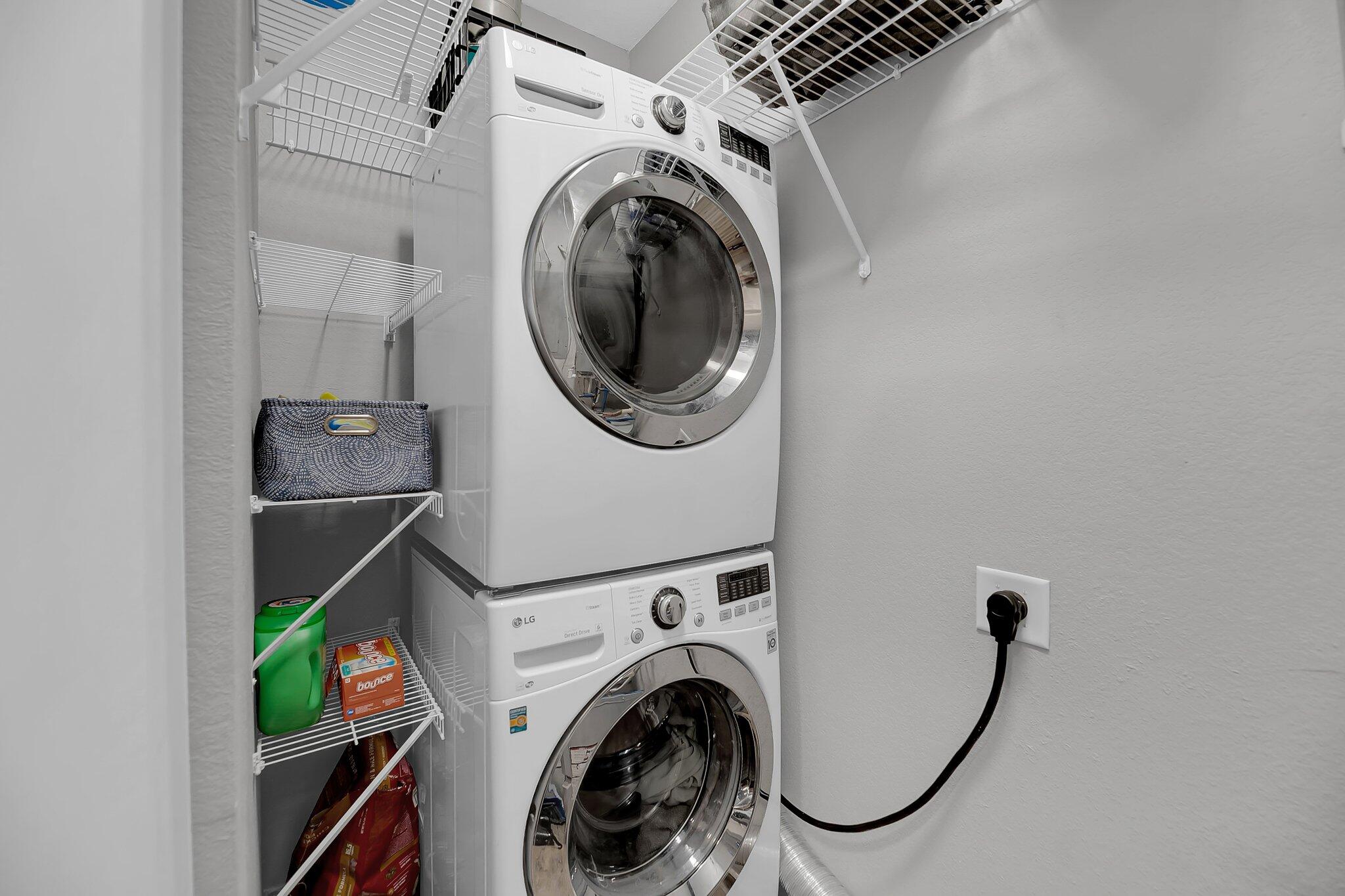 Laundry closet with stacked front-loading washer and dryer beside wire storage shelves.