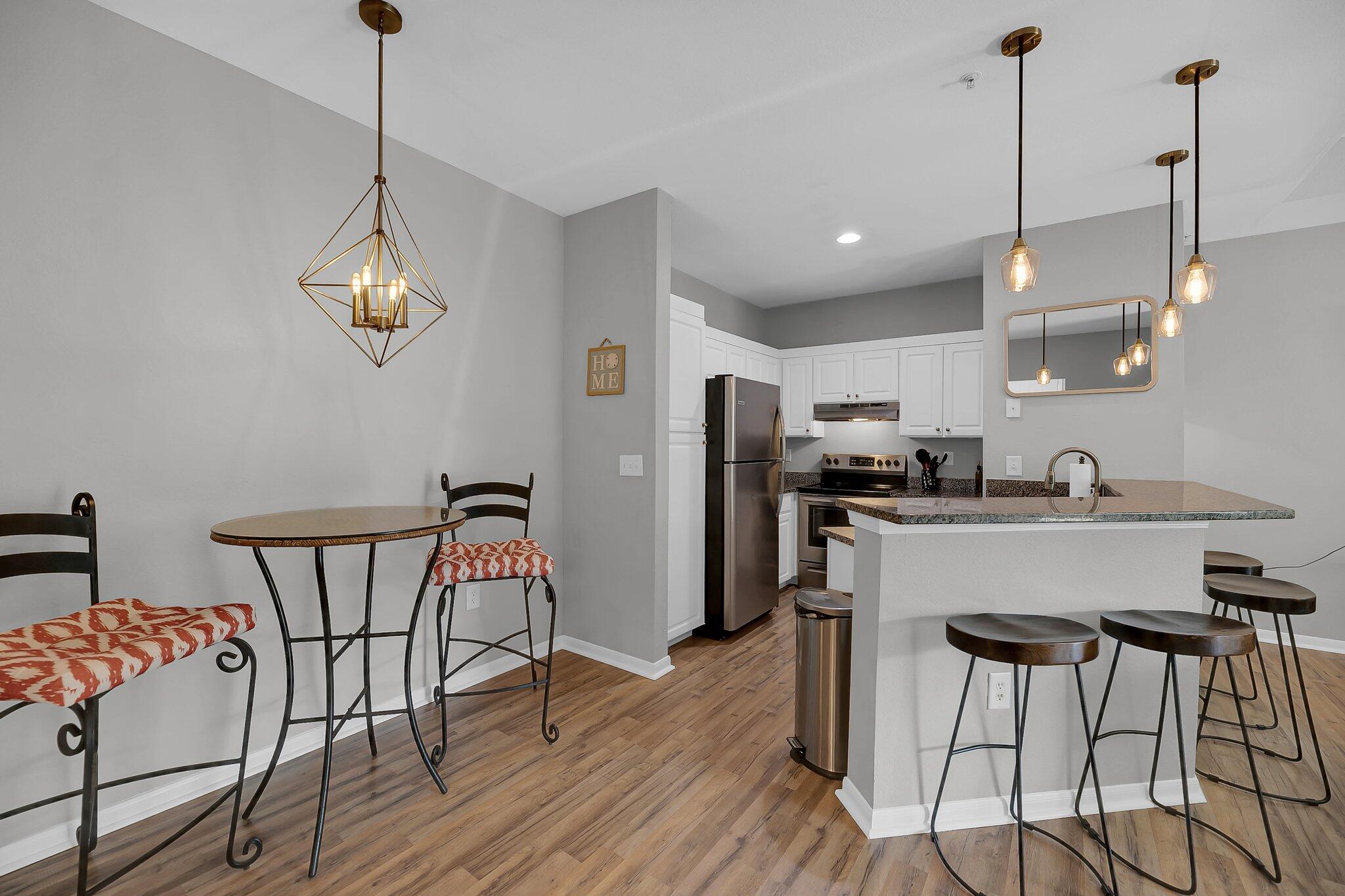 Open kitchen and dining area with a granite island, bar stools, and geometric pendant lights.
