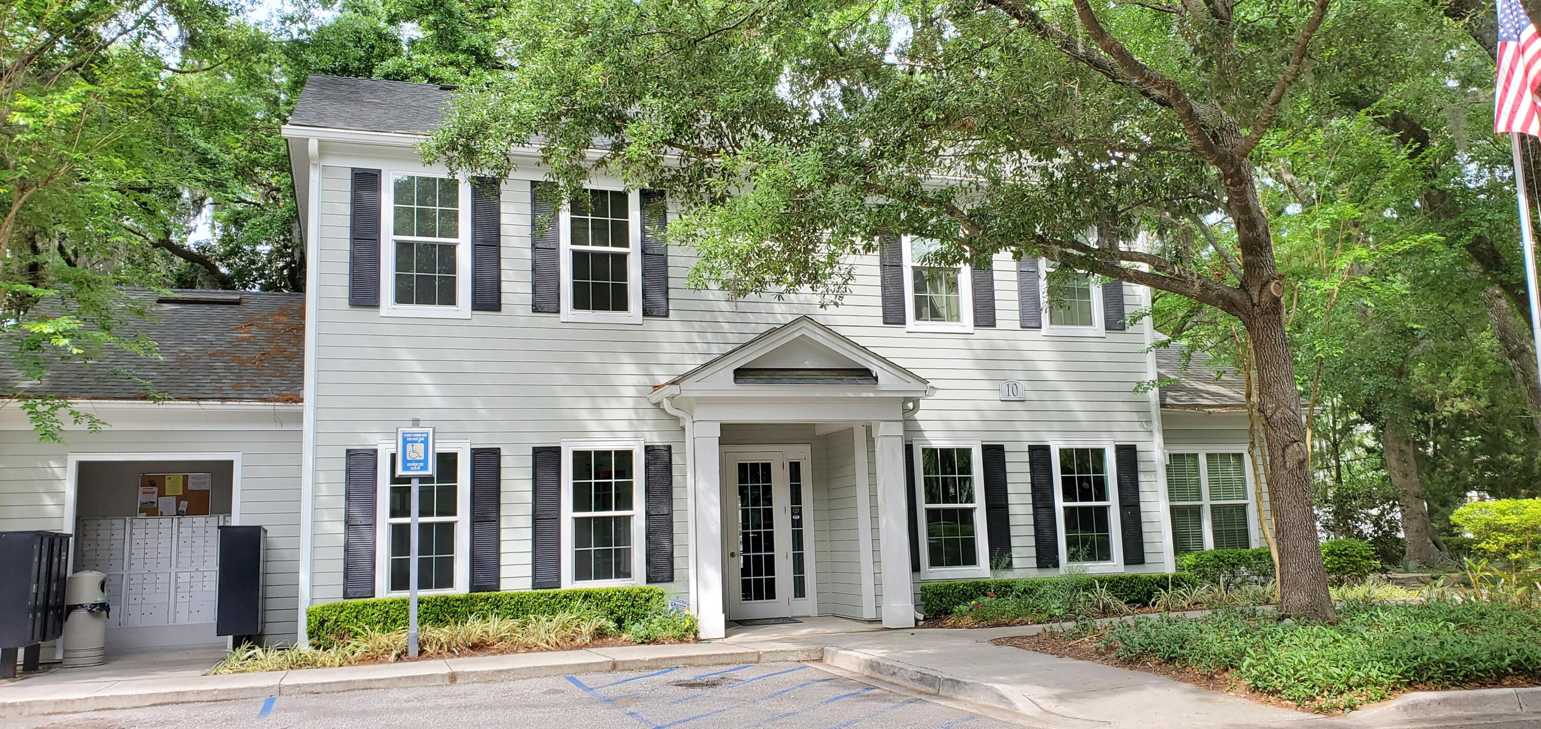 Two-story white residential building with a covered entrance, dark shutters, mature trees, and accessible parking.
