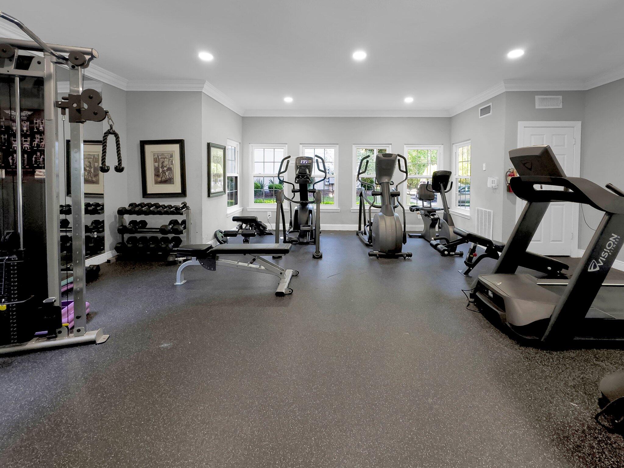 Fitness room with cardio machines, weight equipment, dumbbells, and windows.