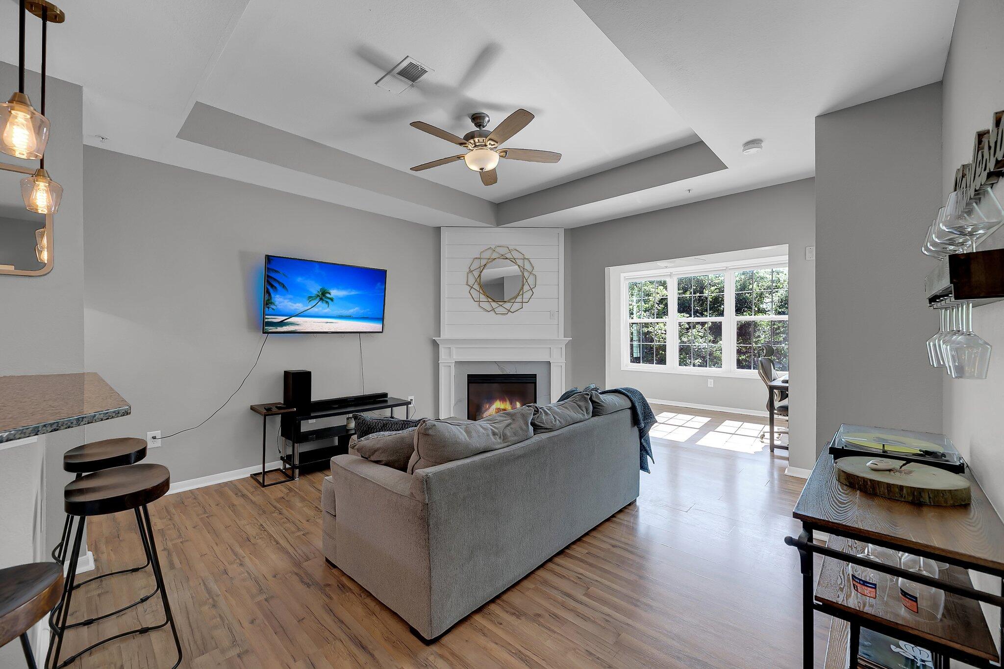 Living room with a gray sofa, white fireplace, tray ceiling, and large sunlit window.