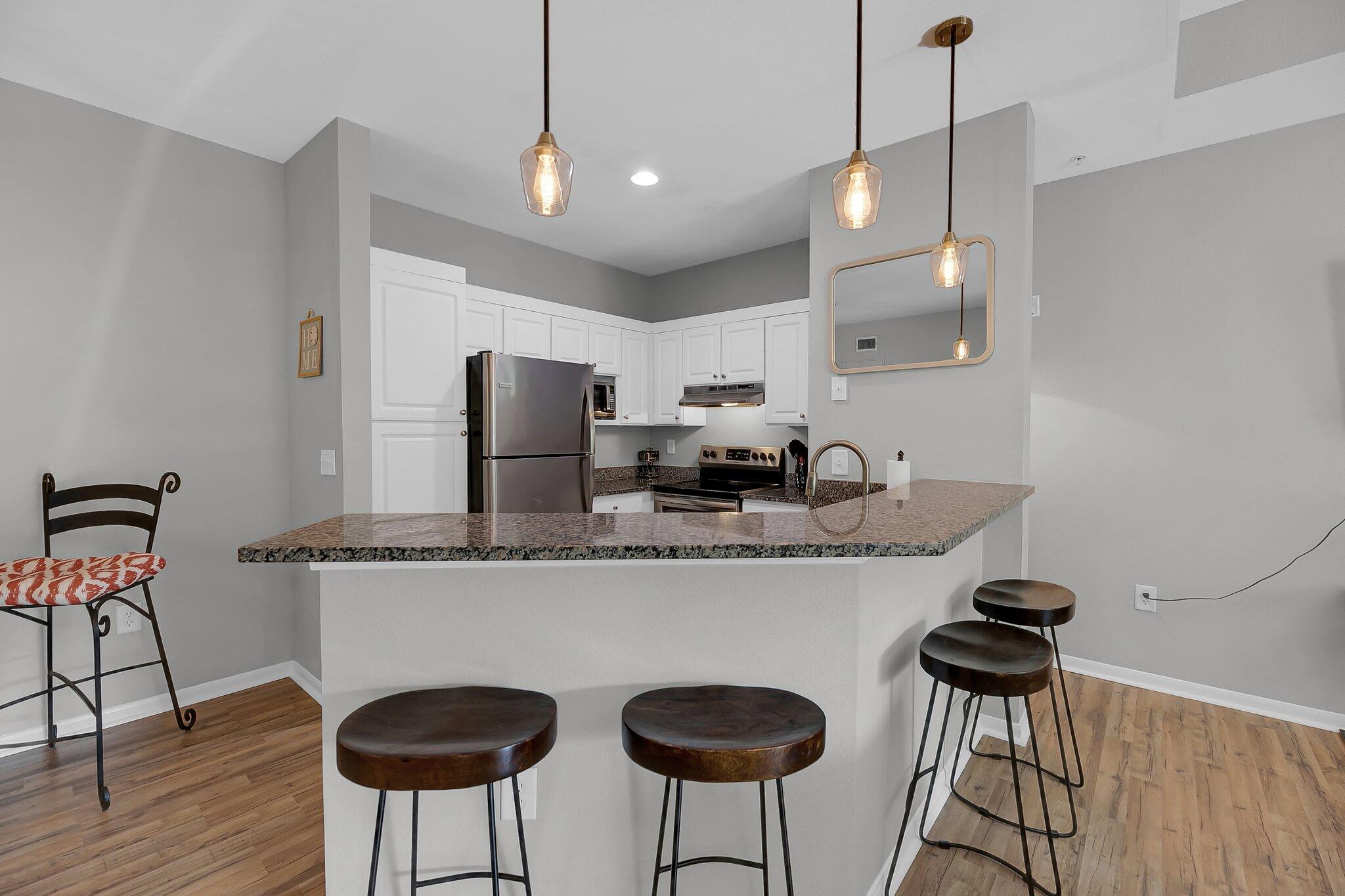 Modern kitchen with a granite breakfast bar, white cabinetry, stainless appliances, and dark wood stools.