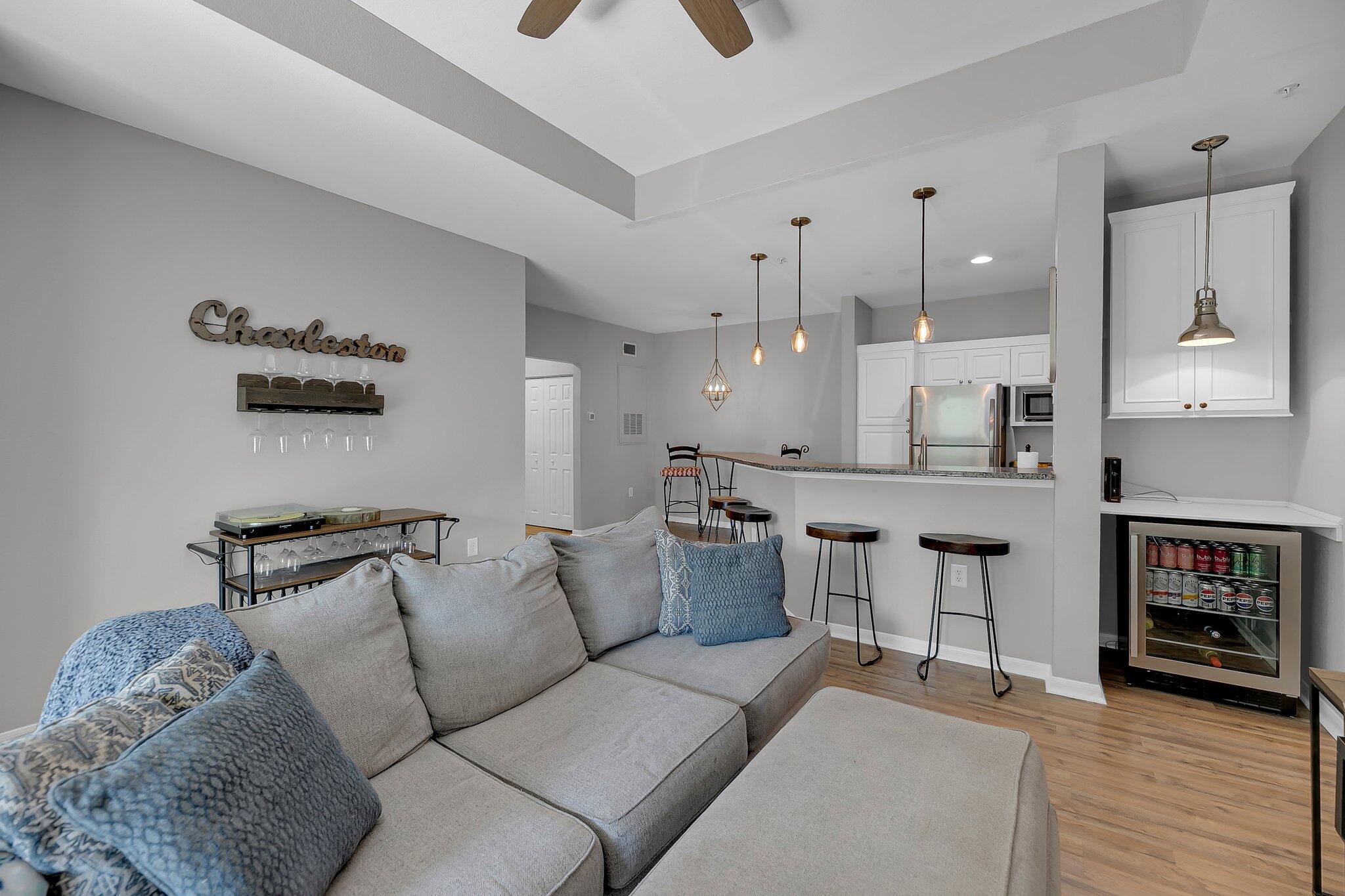 Open-plan living room and kitchen with a gray sectional, blue pillows, and a breakfast bar.