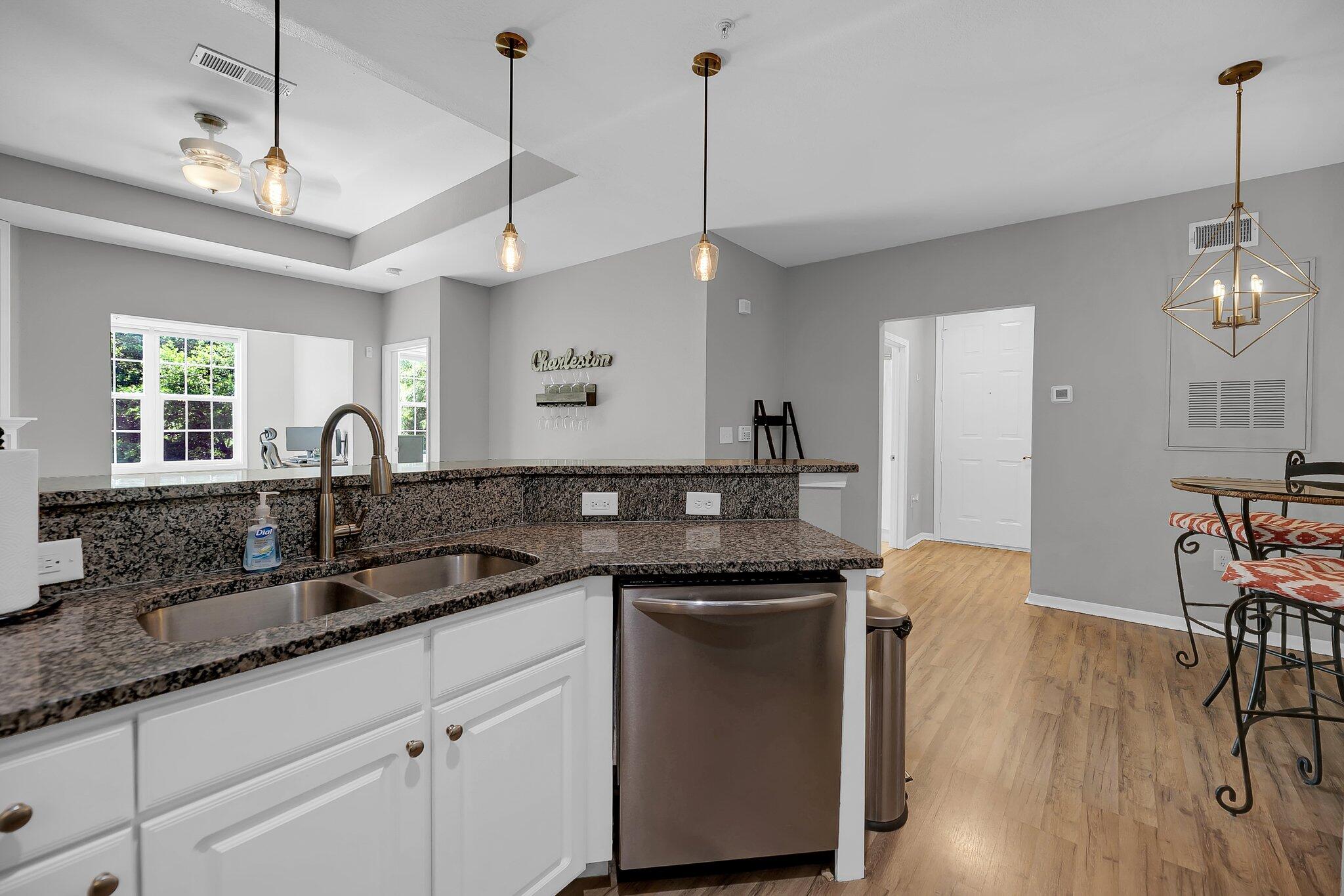 Kitchen with dark granite counters, double sink, stainless dishwasher, and an adjoining dining area.