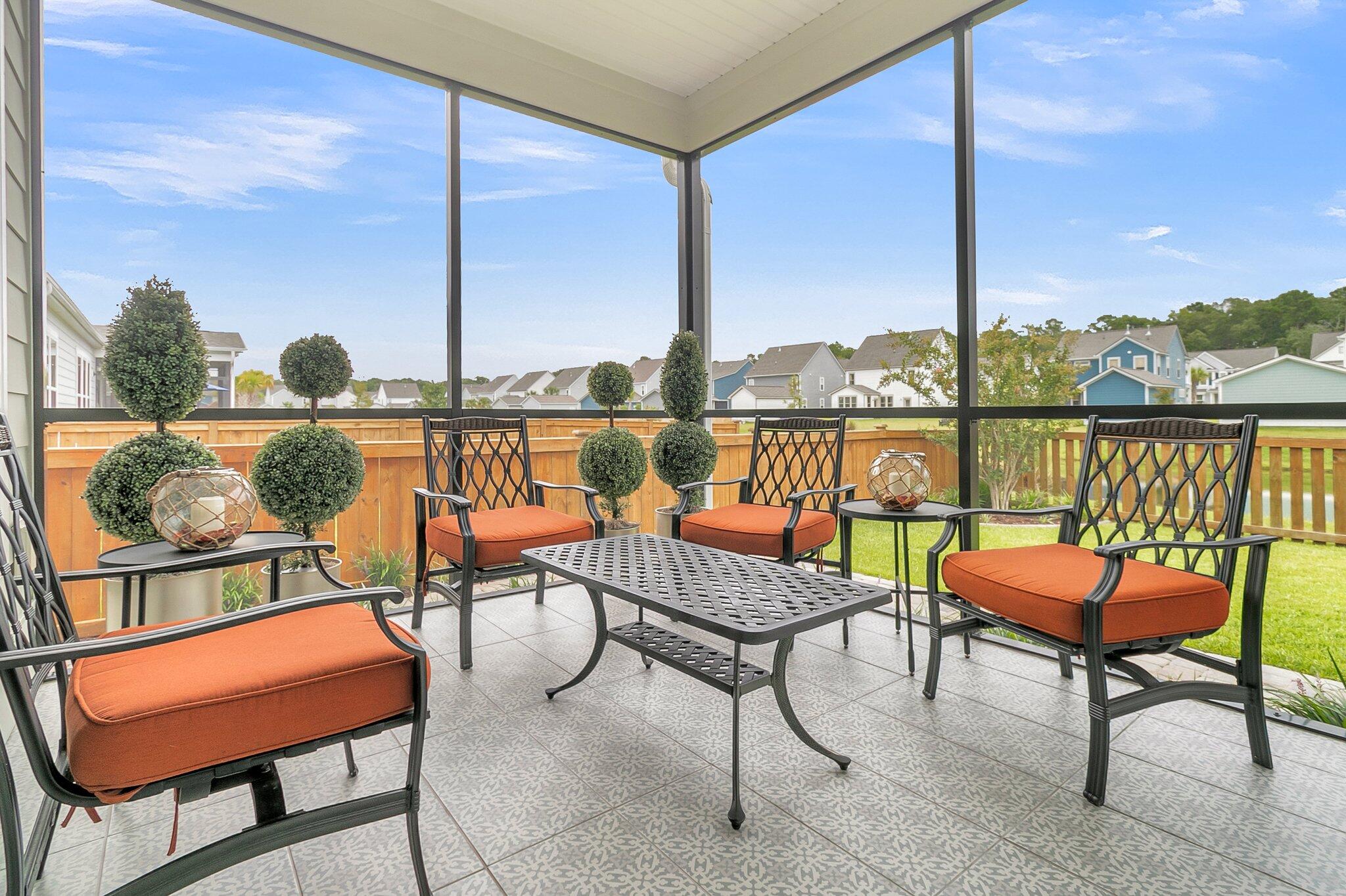 Screened patio with orange-cushioned seating, patterned tile floor, and views of the fenced yard and neighboring homes.