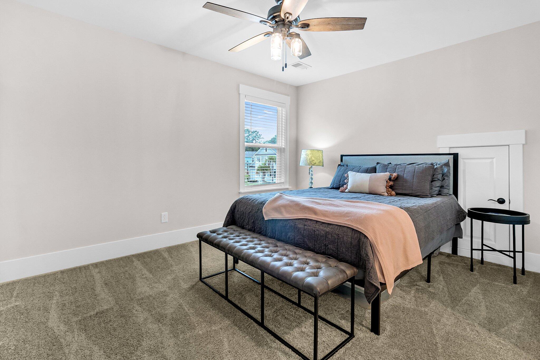 Staged bedroom with a gray bed, blush throw, tufted bench and bright window.