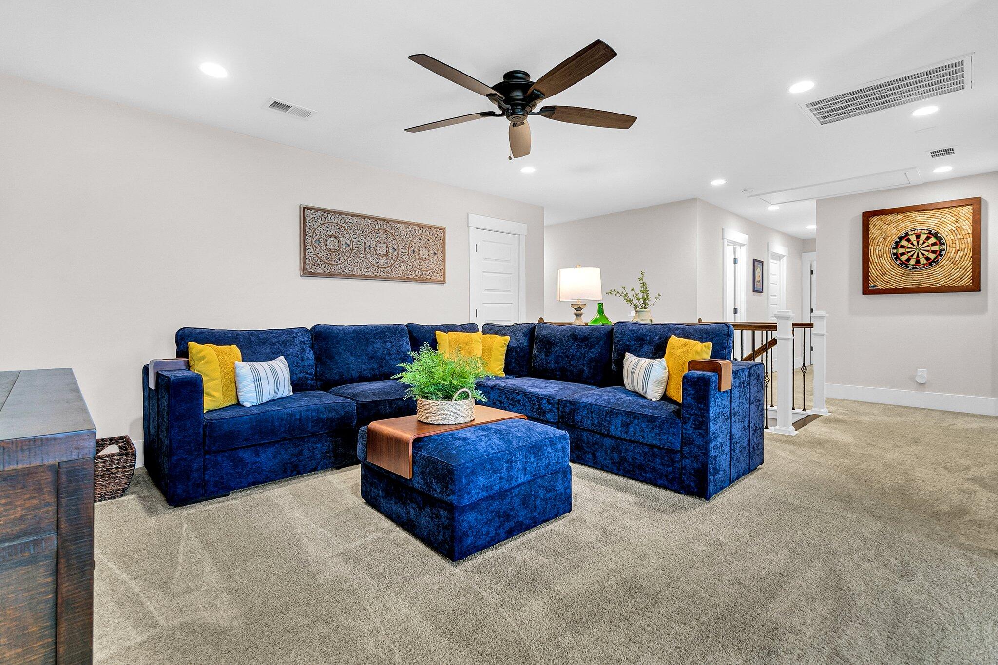Living room with a navy sectional, colorful pillows, matching ottoman, and dartboard wall art.