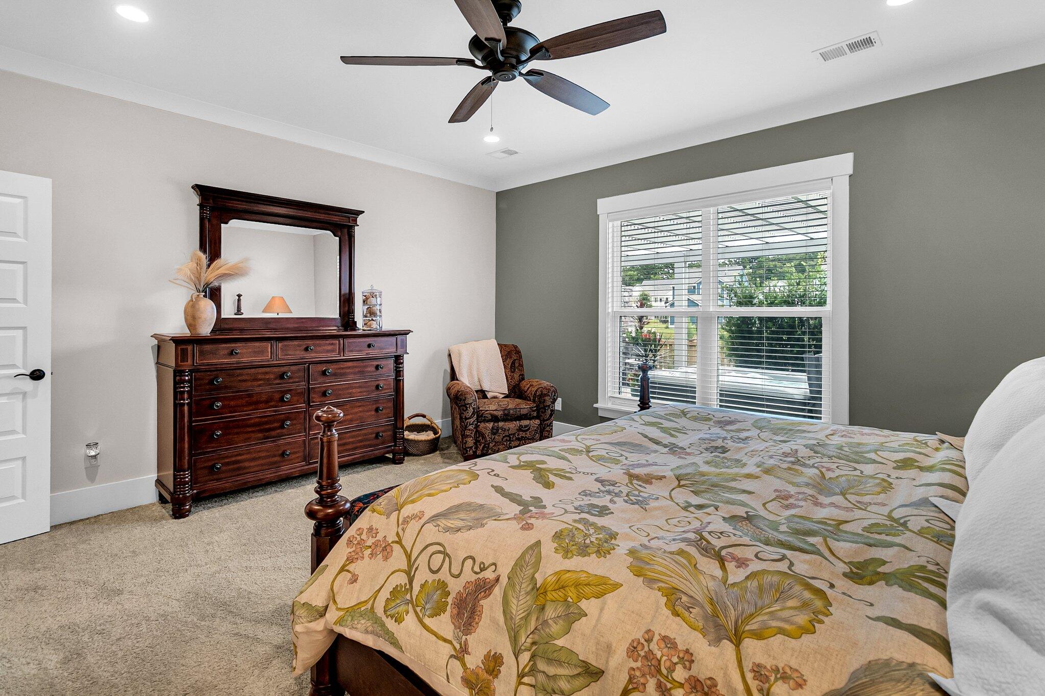 Furnished bedroom with a dark wood dresser, patterned bedspread, and window with white blinds.