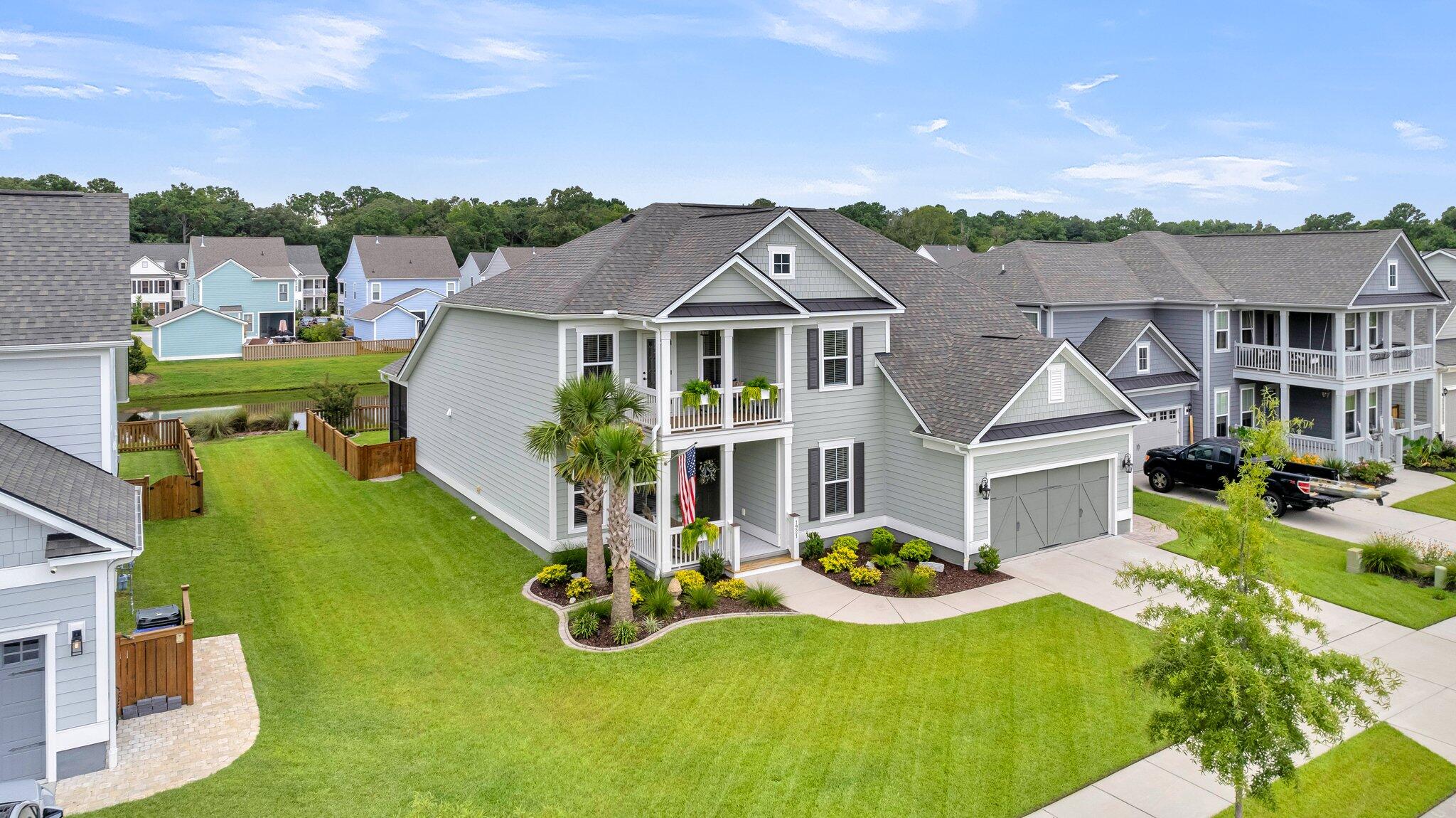Gray two-story home with covered porches, attached garage, and broad lawn among neighboring houses.