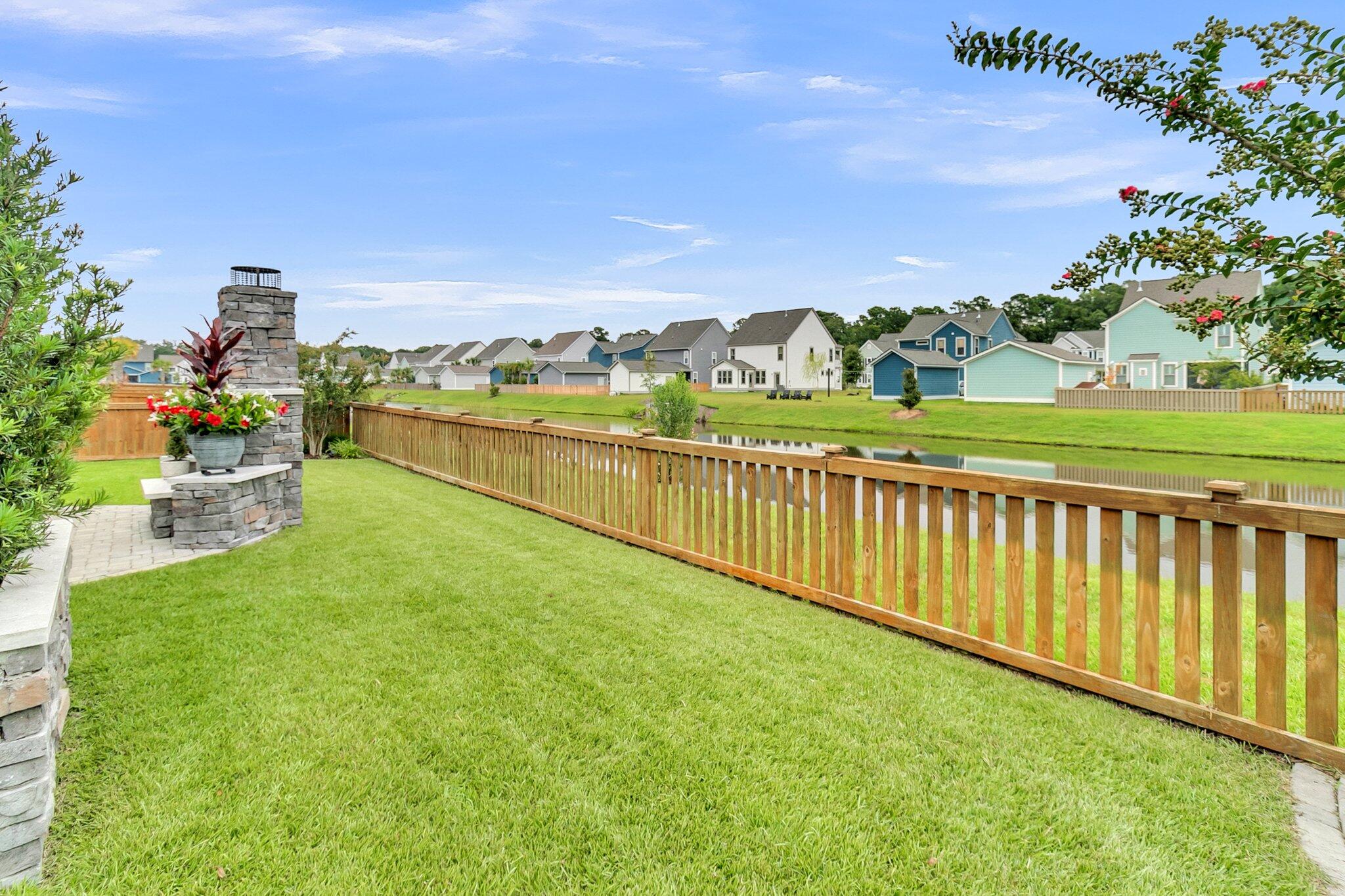 Backyard lawn and stone outdoor fireplace overlook a pond, with neighboring homes across the water.