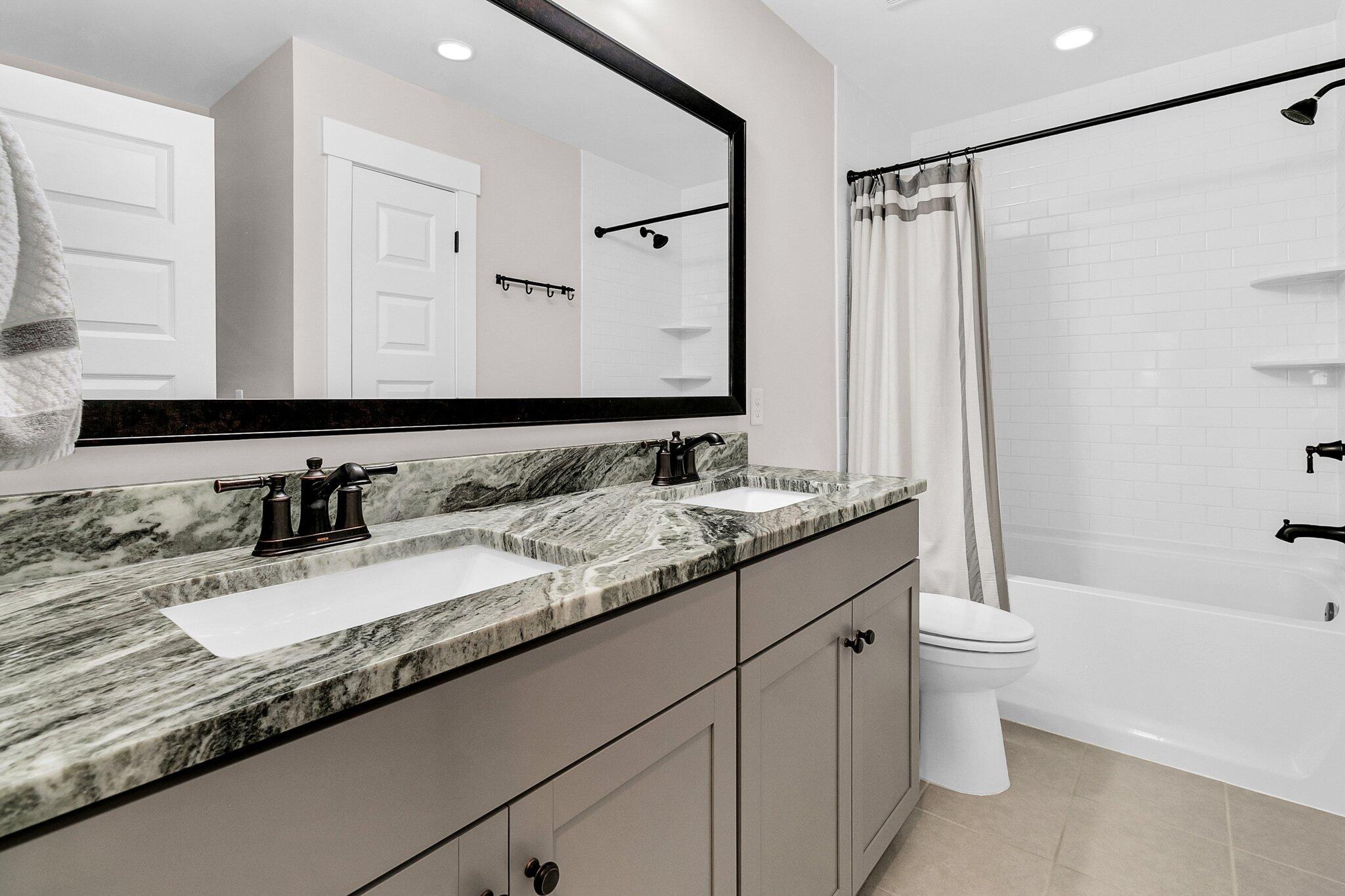 Bathroom with a double vanity, veined stone countertop, and white subway-tile tub and shower.