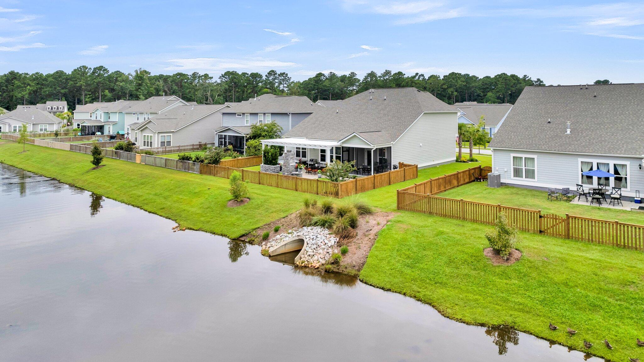 Aerial view of a home with a covered patio and fenced lawn beside a waterway.