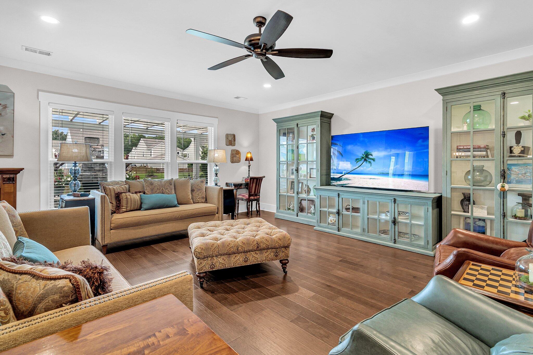 Living room with sage-green display cabinets, brown seating, patterned ottoman, and dark wood floors.