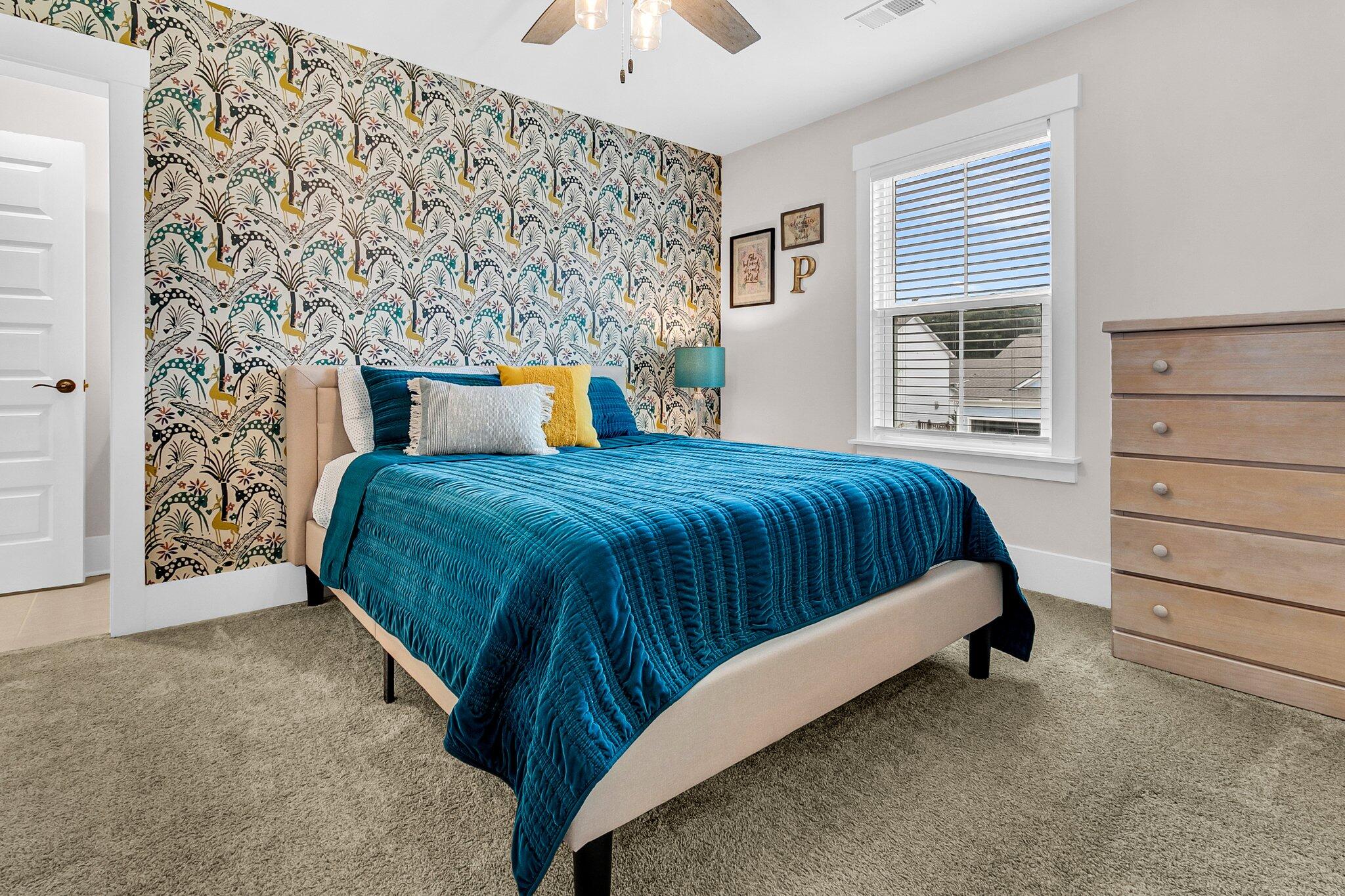 Furnished bedroom with a teal-quilted bed and colorful patterned wallpaper.