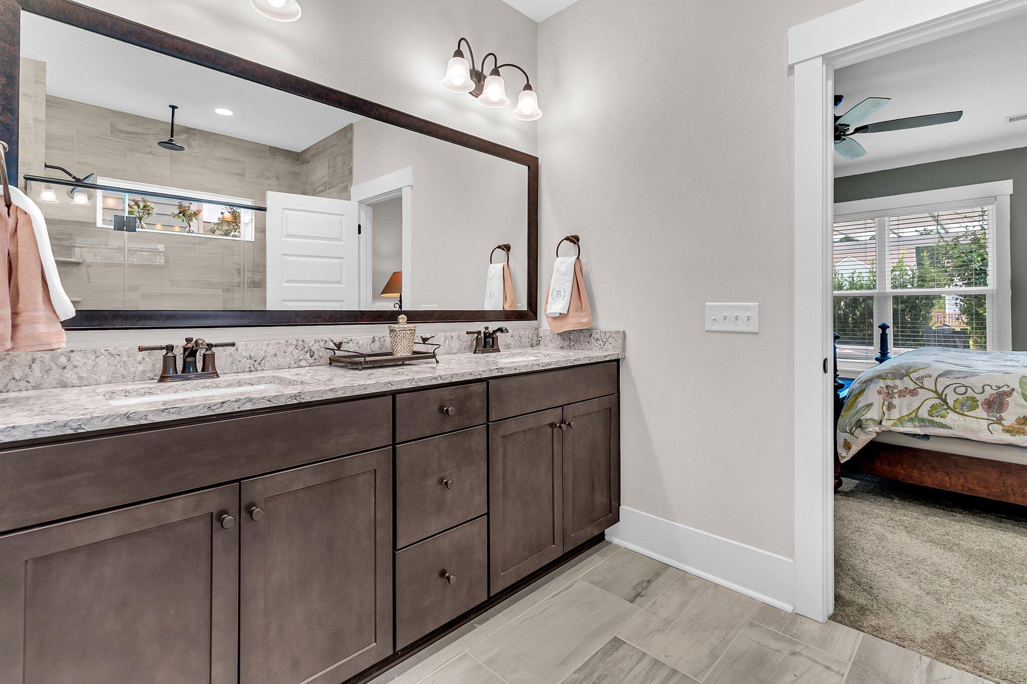 Bathroom with a double-sink dark wood vanity, stone countertop, and doorway to a bedroom.