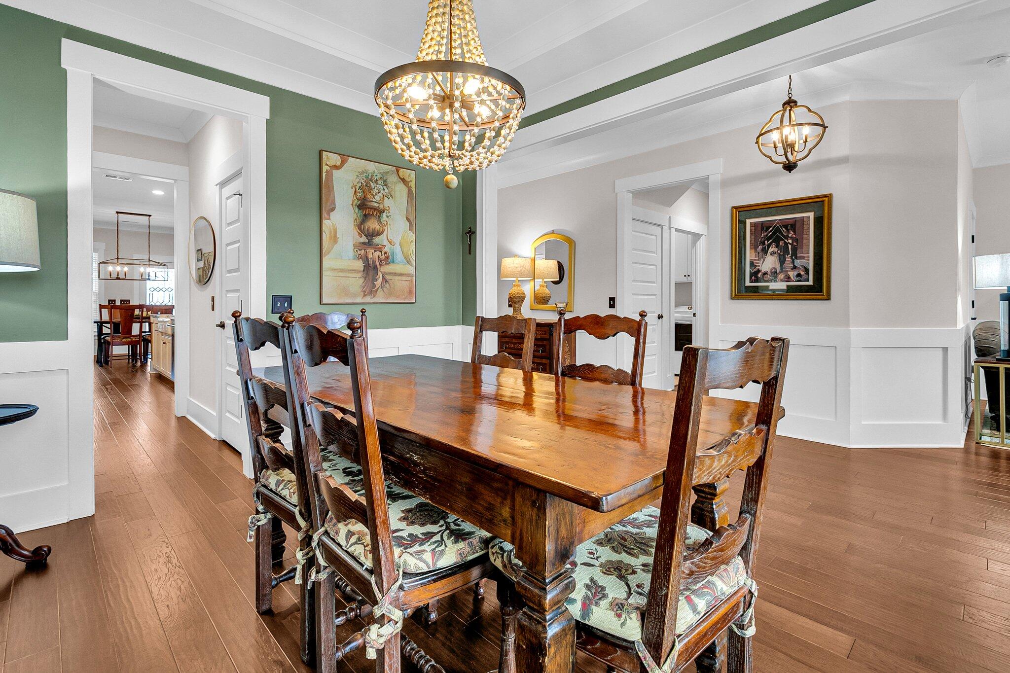 Dining room with a rustic wooden table, carved chairs, green accent wall, and beaded chandelier.