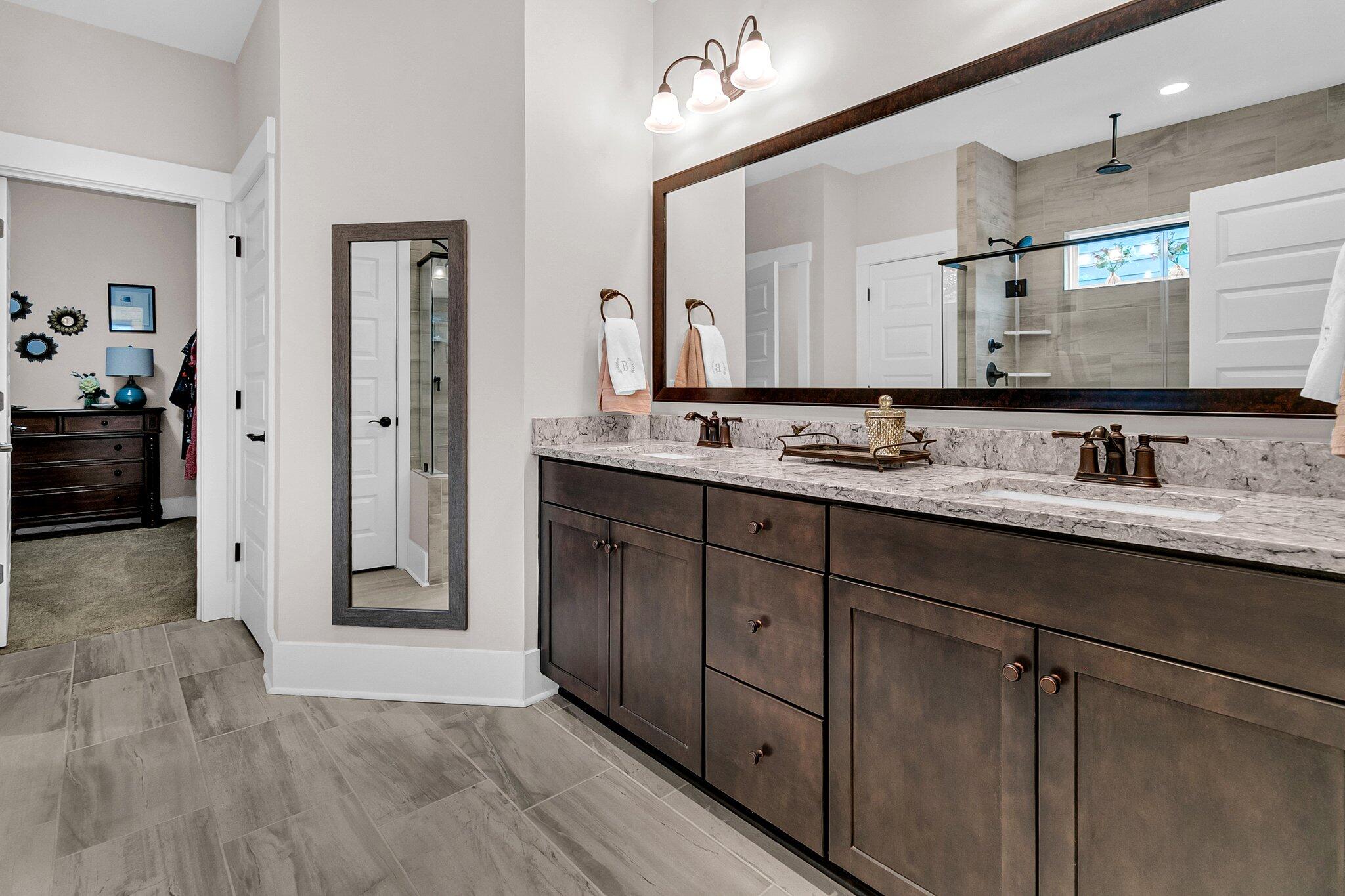 Bathroom with a dark double vanity, large framed mirror, and glass-enclosed tiled shower.