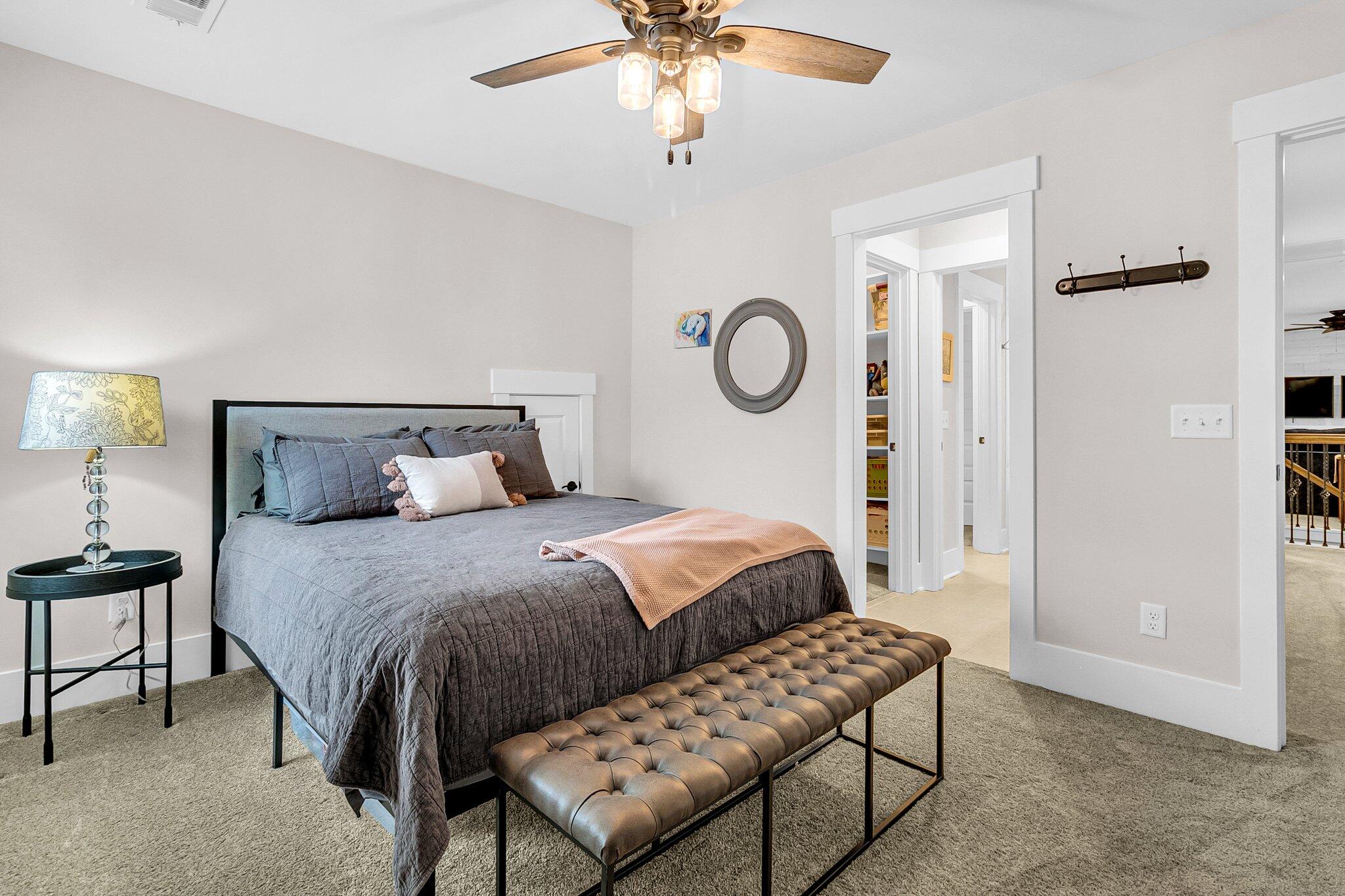 Staged bedroom with gray bedding, a blush throw, and a tufted leather bench at the foot of the bed.