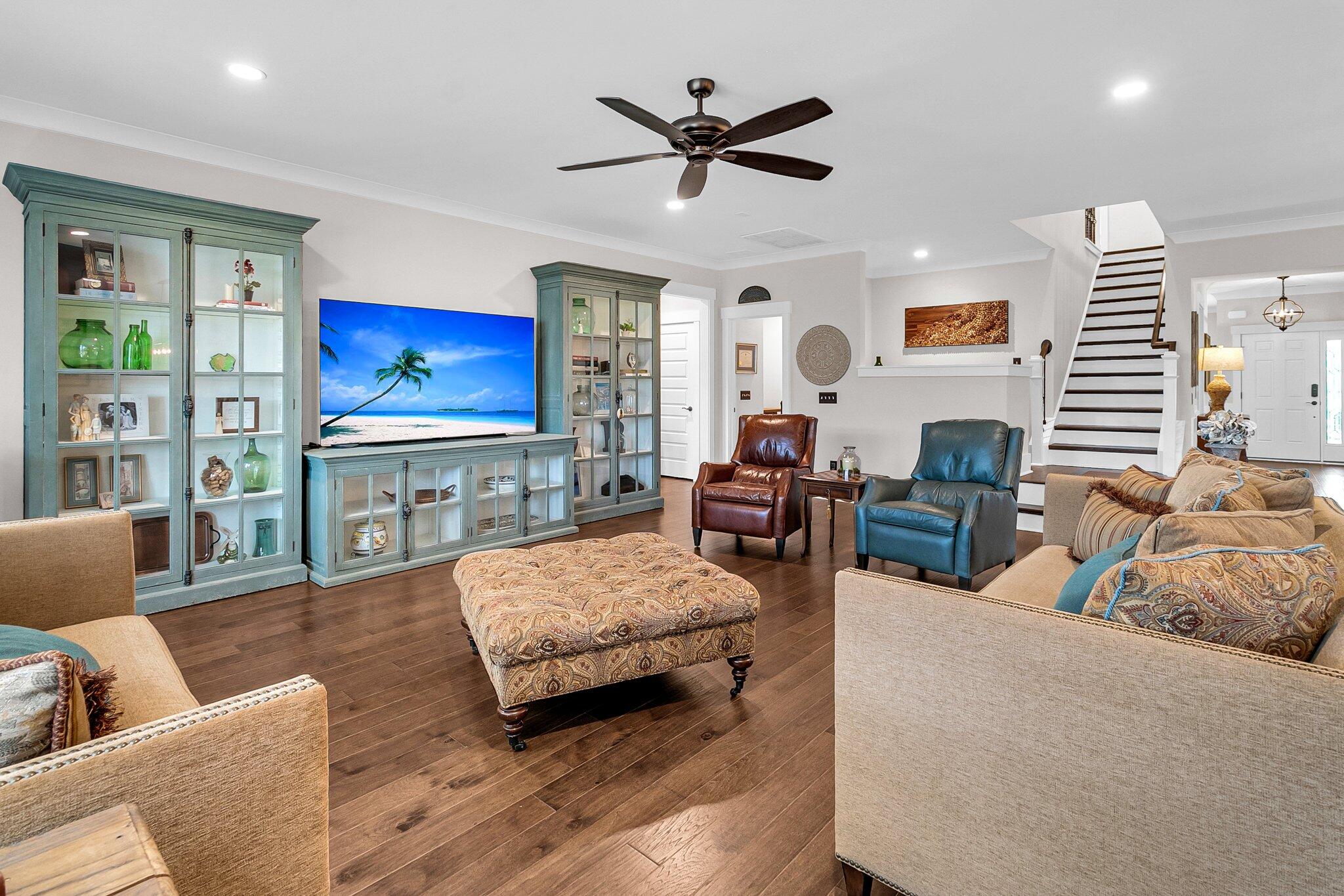 Furnished living room with teal display cabinets, leather chairs, and dark wood floors.