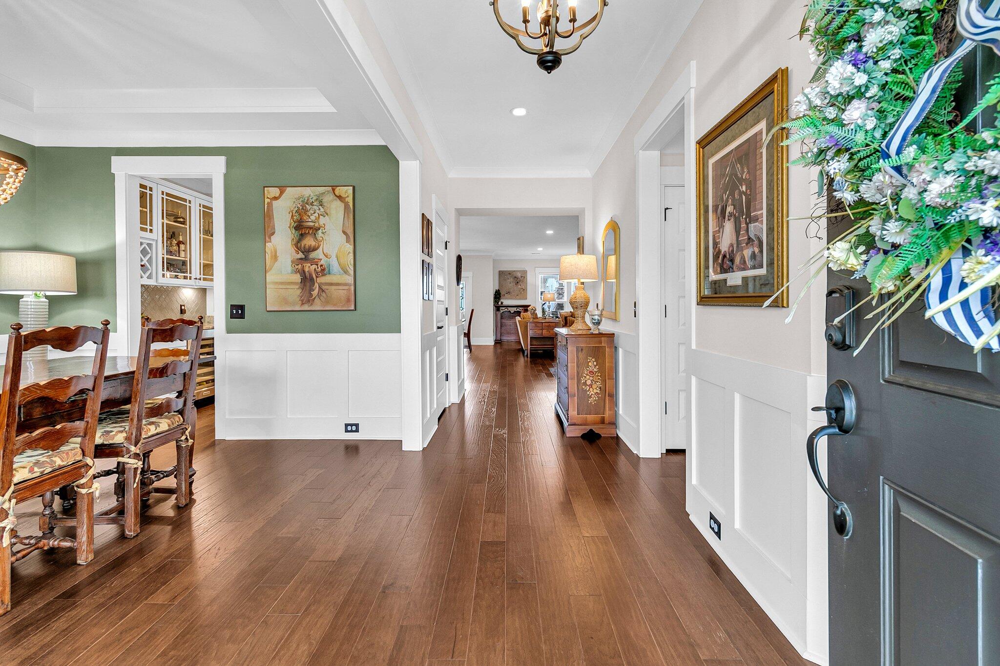 Entry hall with dark wood floors, white wainscoting, and a floral wreath on the front door