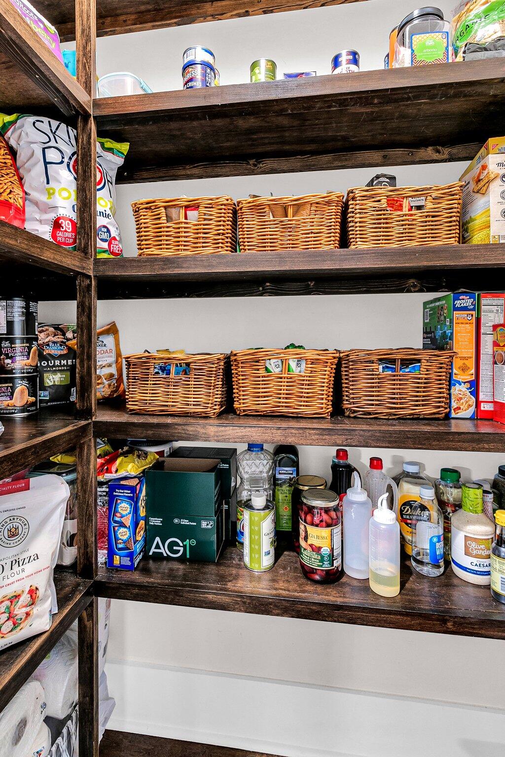 Walk-in pantry with dark wood shelves, wicker baskets, and neatly arranged groceries.