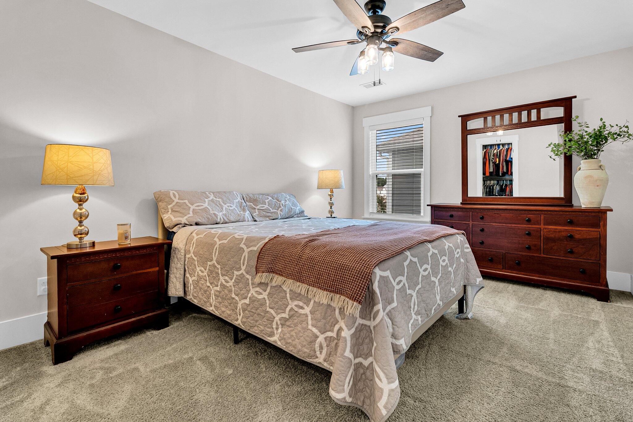 Furnished bedroom with a patterned bed, dark wood dresser, and ceiling fan.