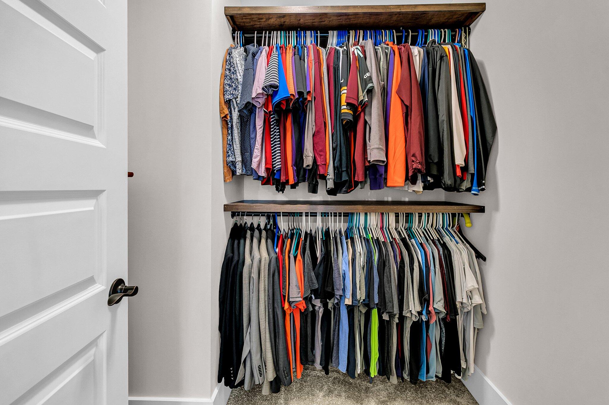 Closet with two rows of hanging clothes and dark wood shelves.