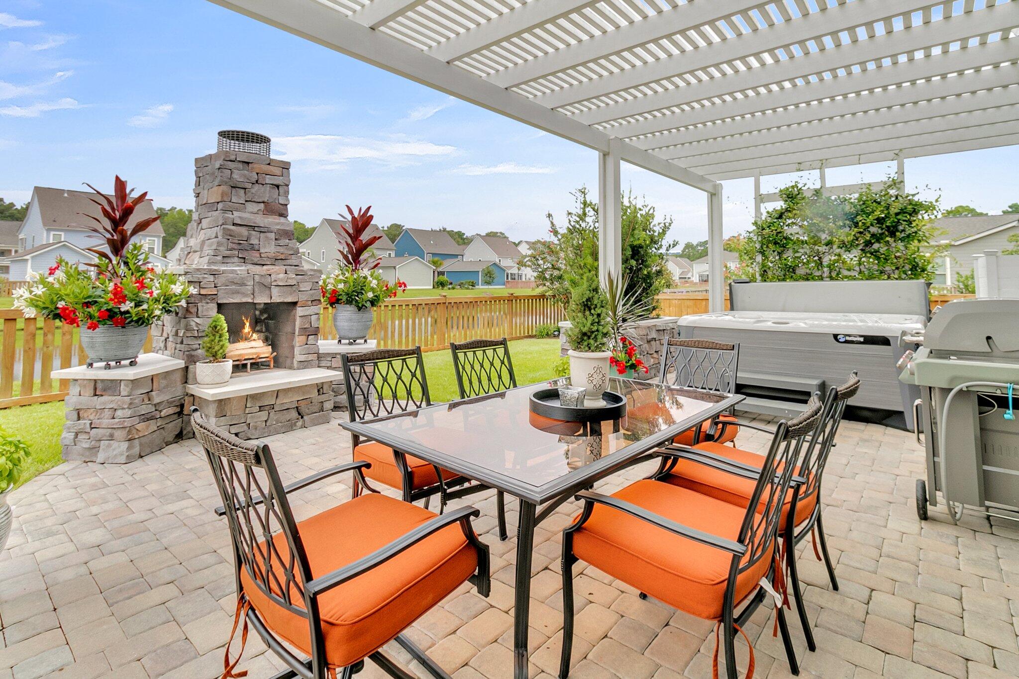 Pergola-covered patio with a stone fireplace, orange-cushioned dining set, hot tub, and grill.