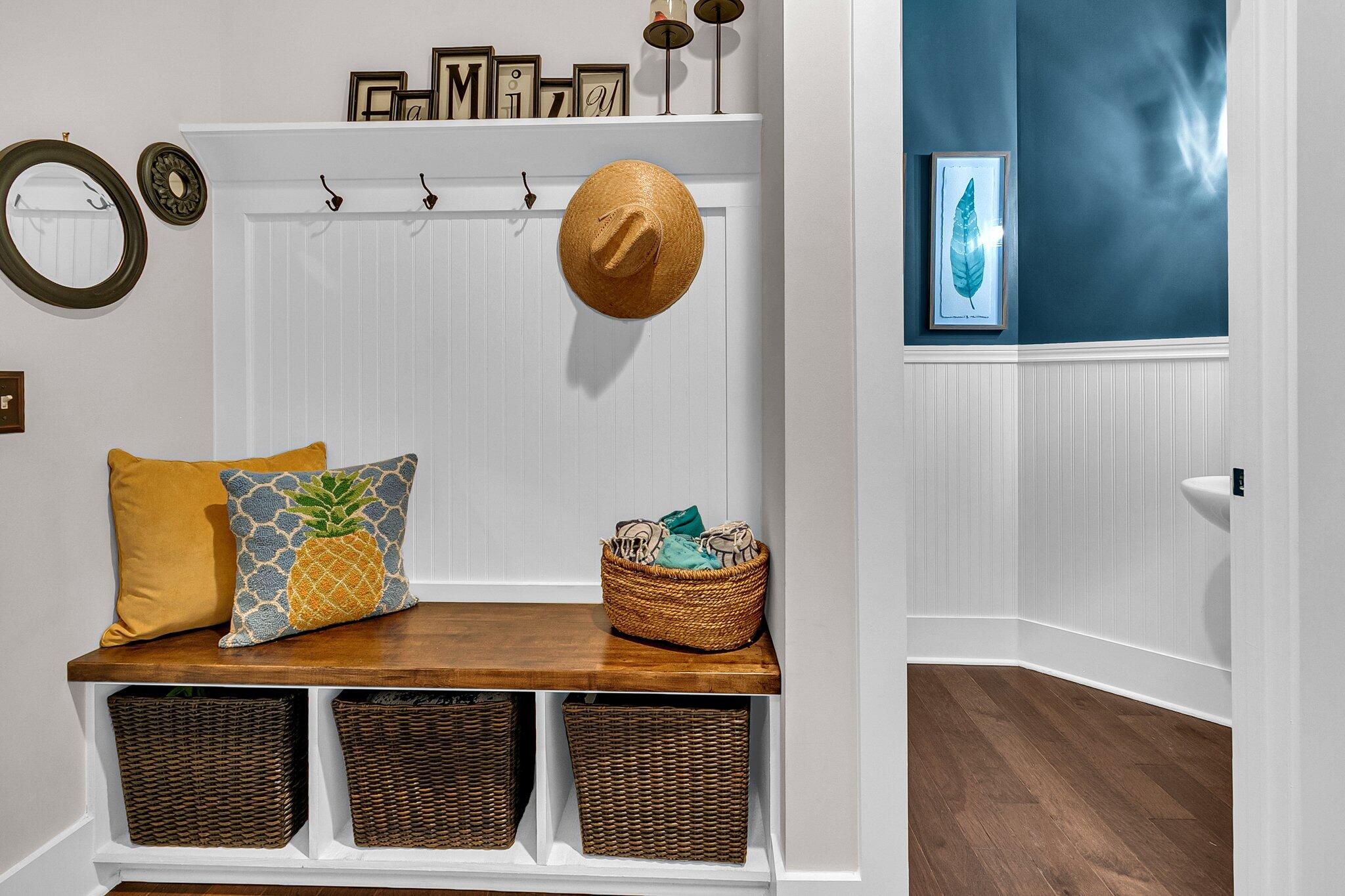 Mudroom bench with woven baskets, decorative pillows, and hooks beside a blue beadboard room.