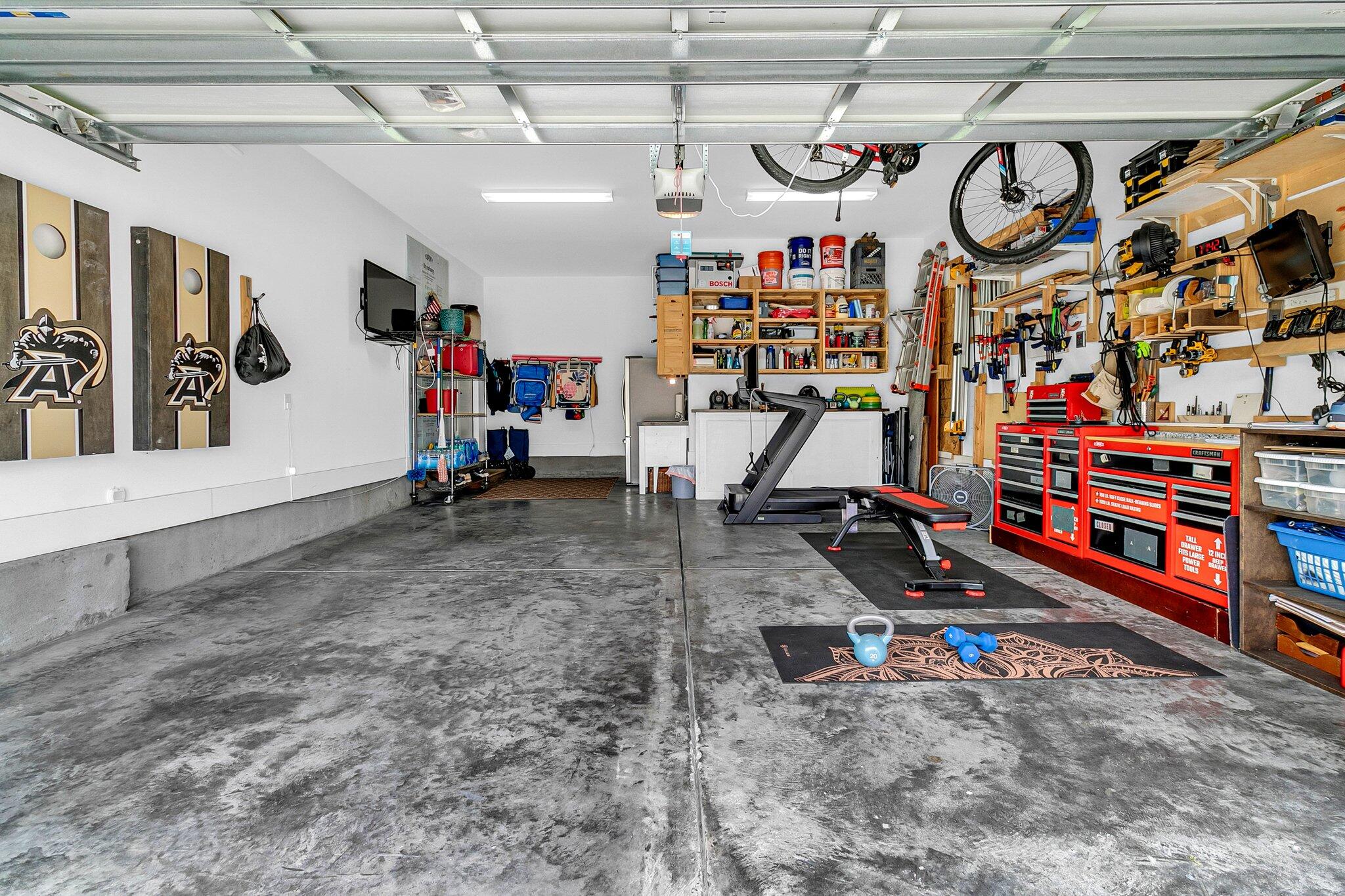 Garage with concrete floors, red tool cabinets, wall-mounted tools, and a workout area.