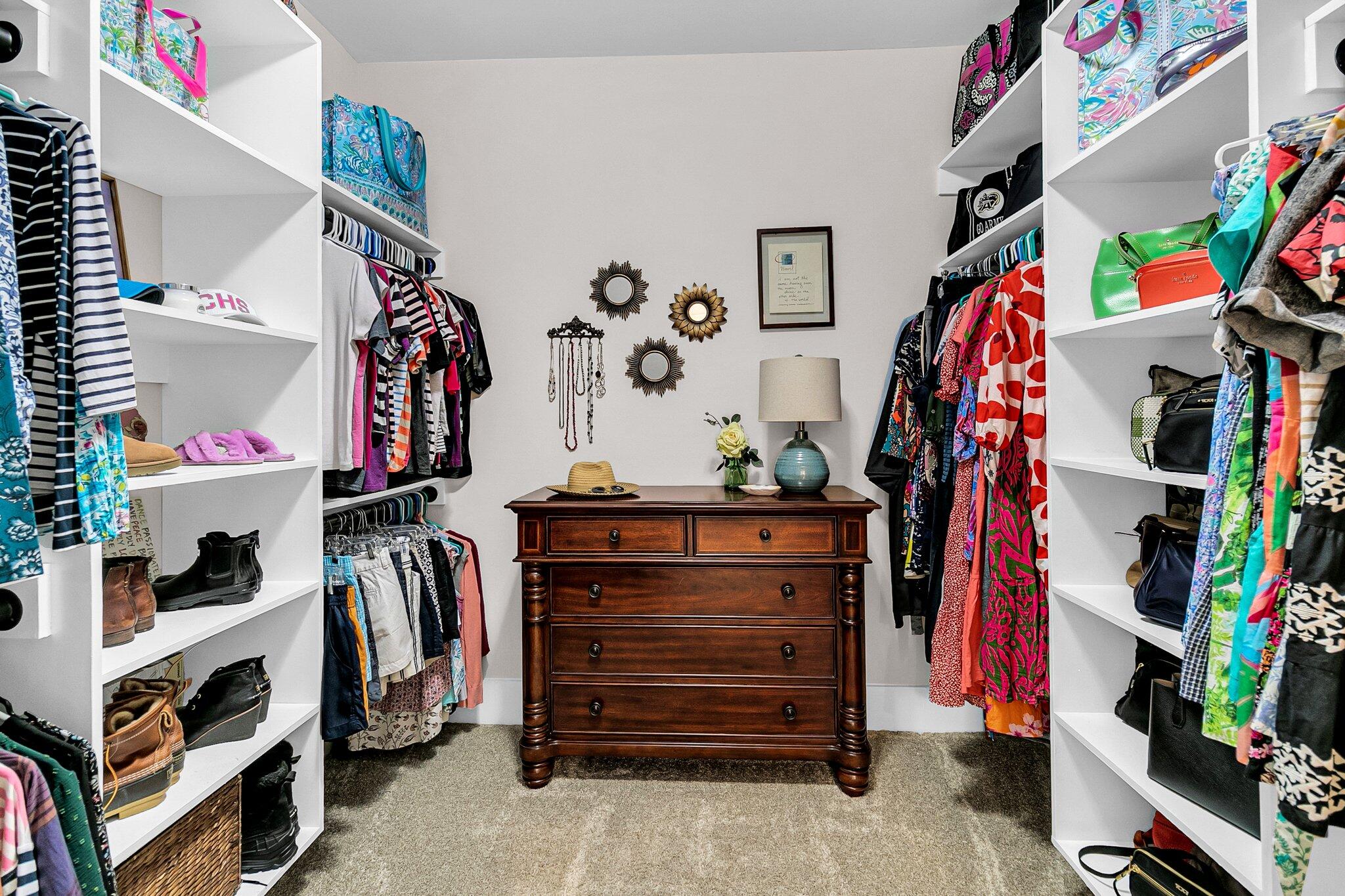 Walk-in closet with colorful clothes and accessories surrounding a dark wood dresser.
