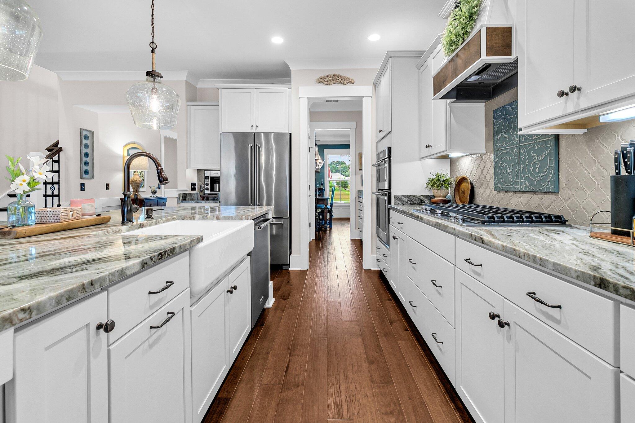 Bright kitchen with white cabinets, marble-patterned counters, farmhouse sink, stainless appliances, and dark wood floors.