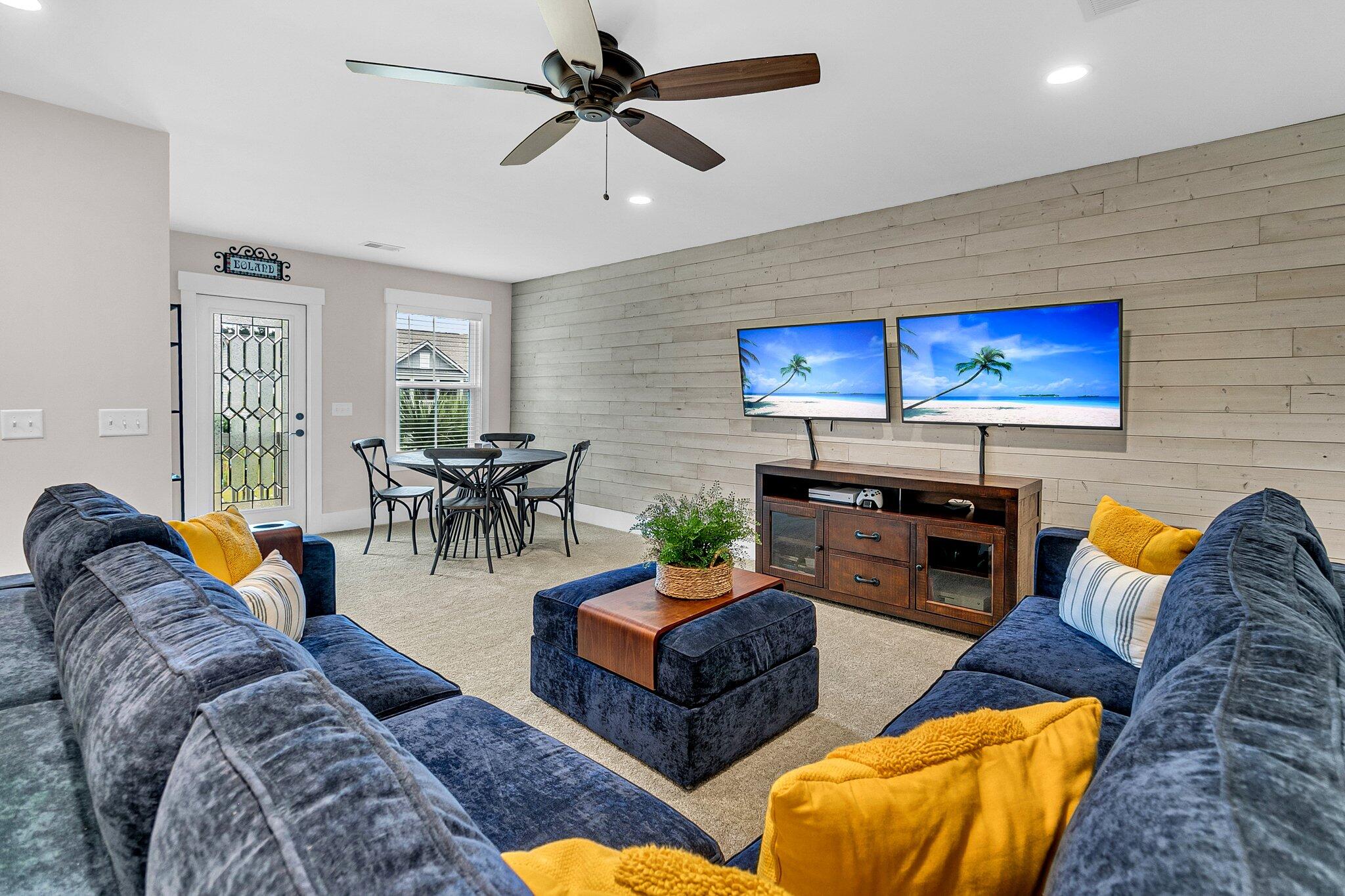 Living room with navy sofas, yellow pillows, a plank accent wall, and a dining area.